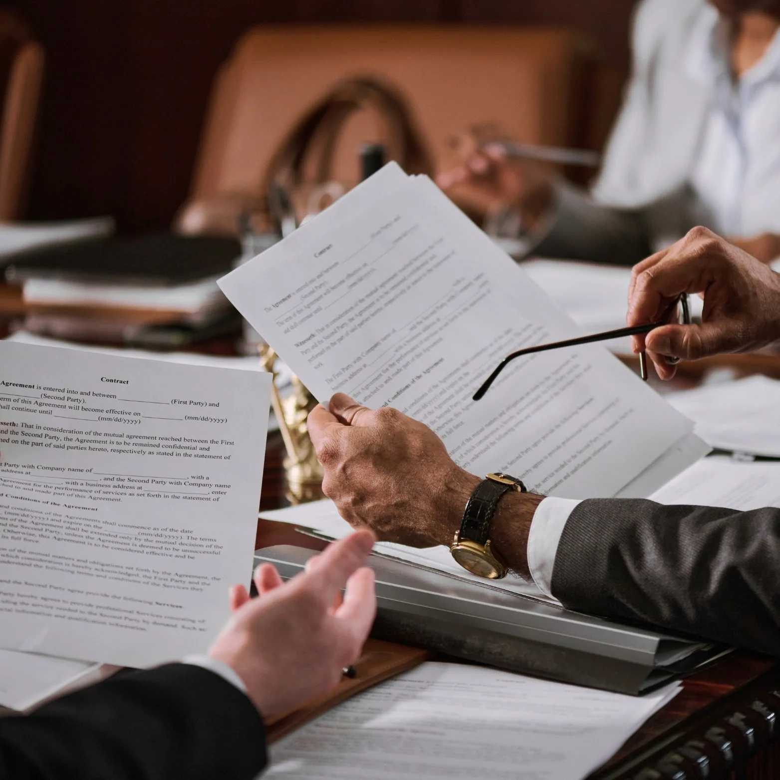 Close-up of hands holding legal documents during a business meeting with others visible in the background.