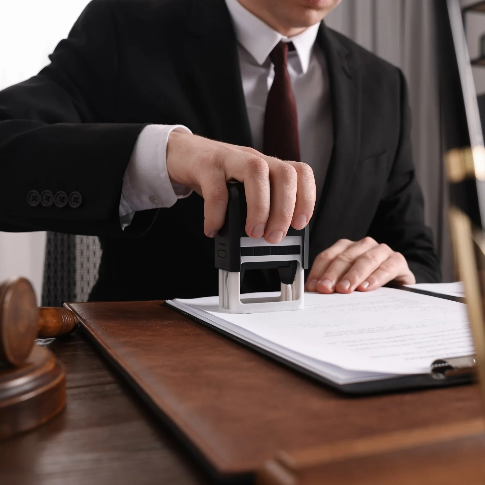 A person in formal attire using a stamp on a document at a desk.