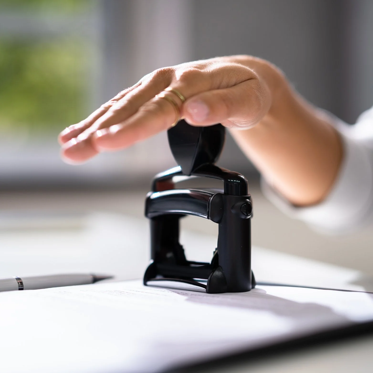 Close-up of a hand pressing a staple gun onto a sheet of paper on a desk.