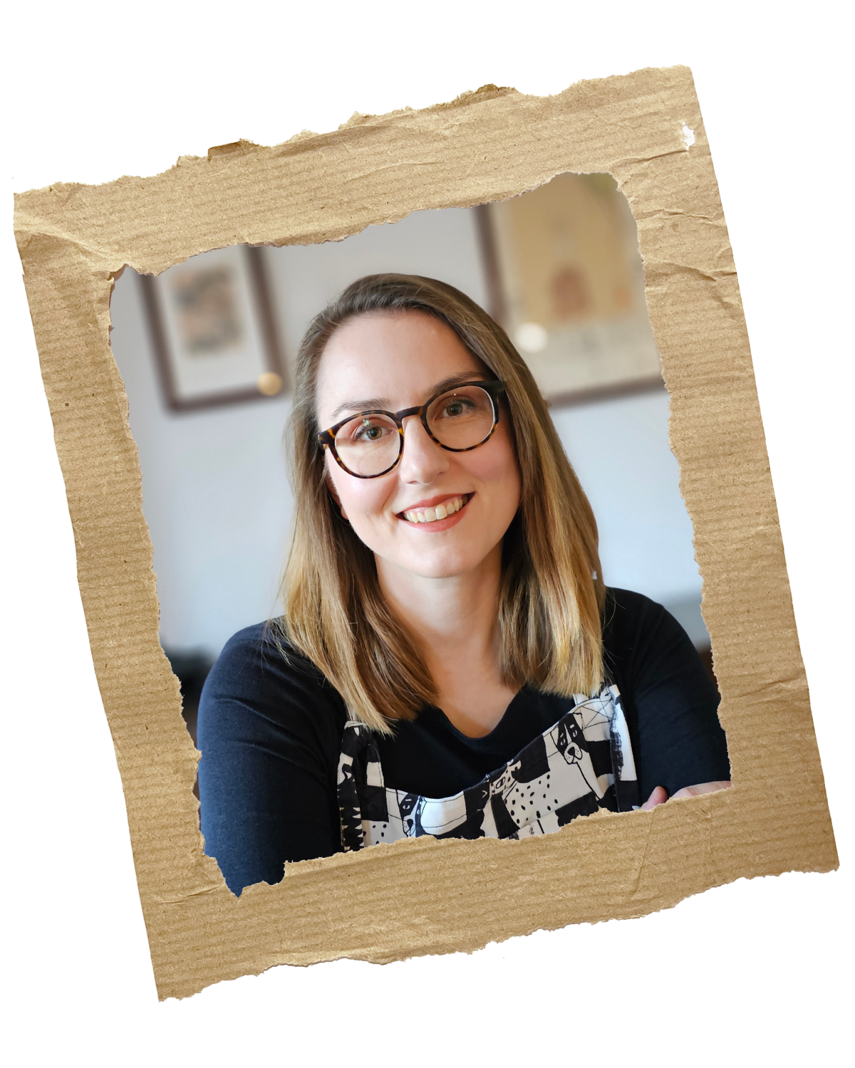 Anikó smiling at the camera, wearing a black long-sleeve t-shirt and a pair of black and white ungarees with cats and dogs. Her hair is dark blond, a bit longer than shoulder-length, and she is also wearing glasses.