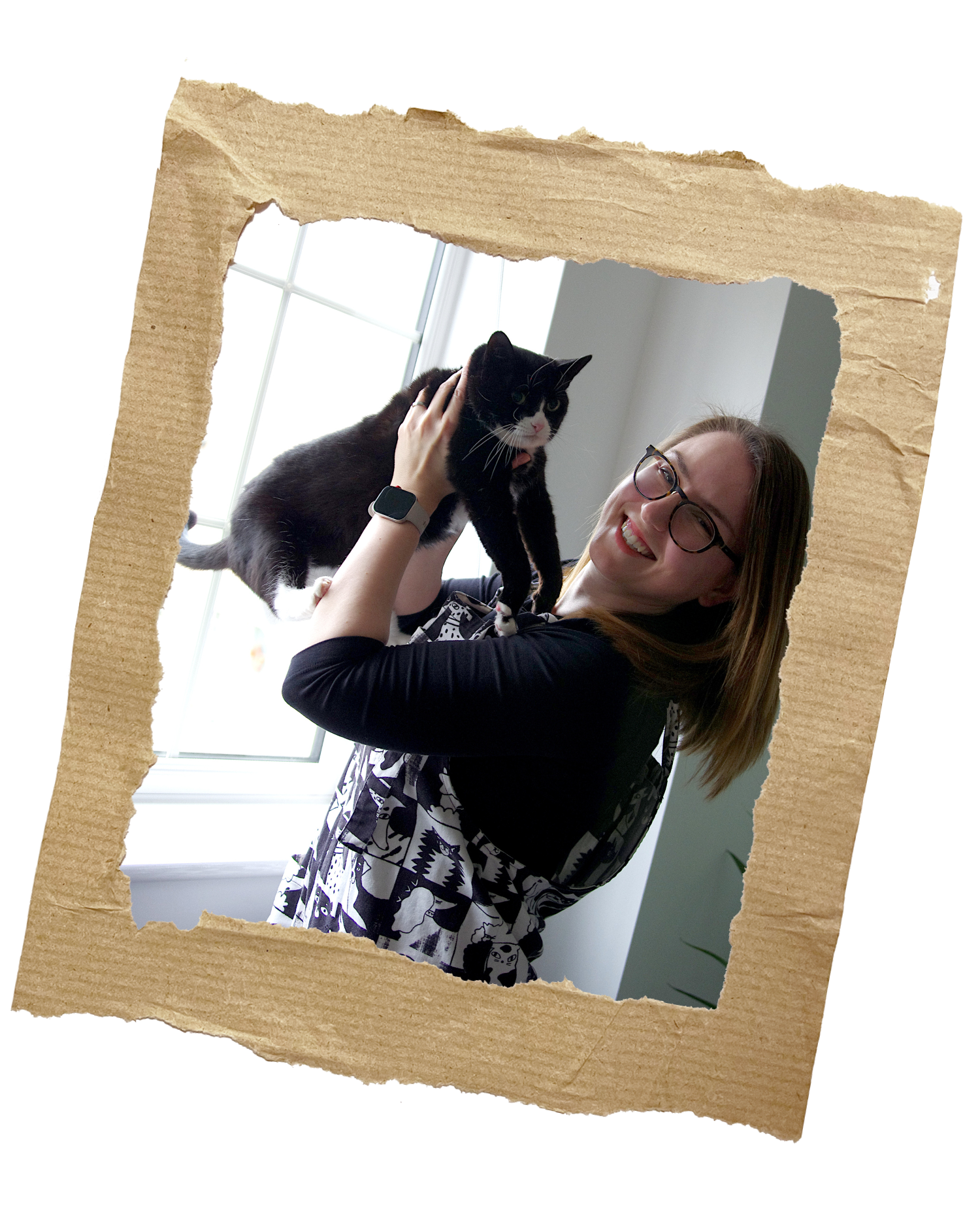 Anikó and her tuxedo cat, Pip are being silly in front of a window.