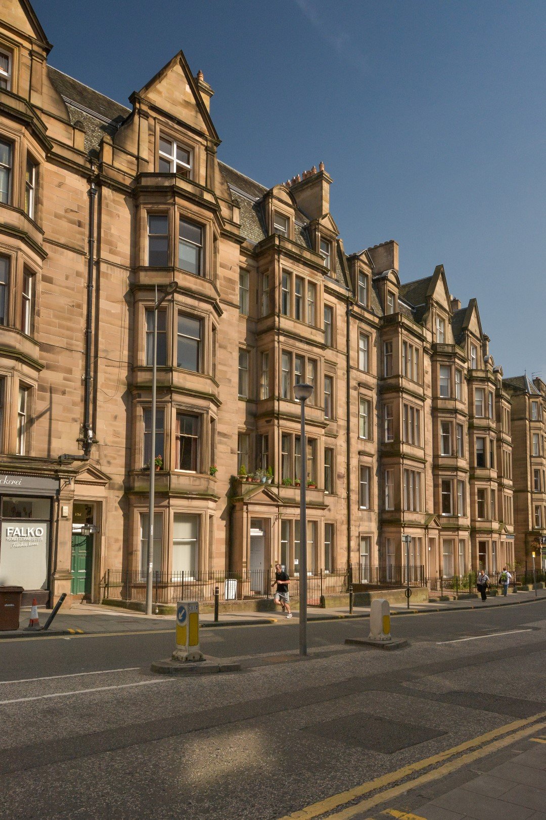 Historic sandstone apartment building with bay windows and gabled roofs on a city street.