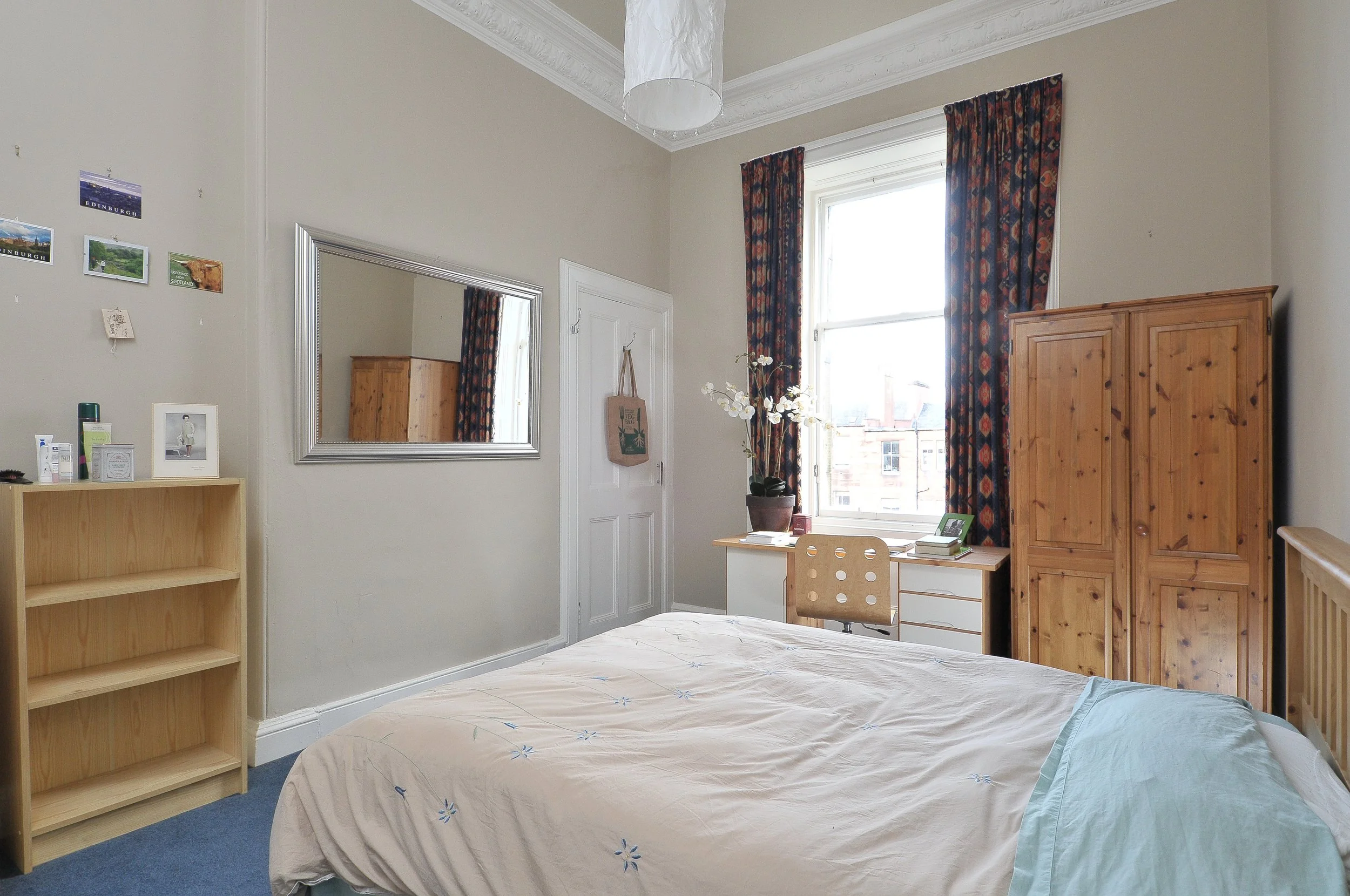 Modern wooden house on a grassy landscape with small trees near a lake, with mountains in the background under a cloudy sky.