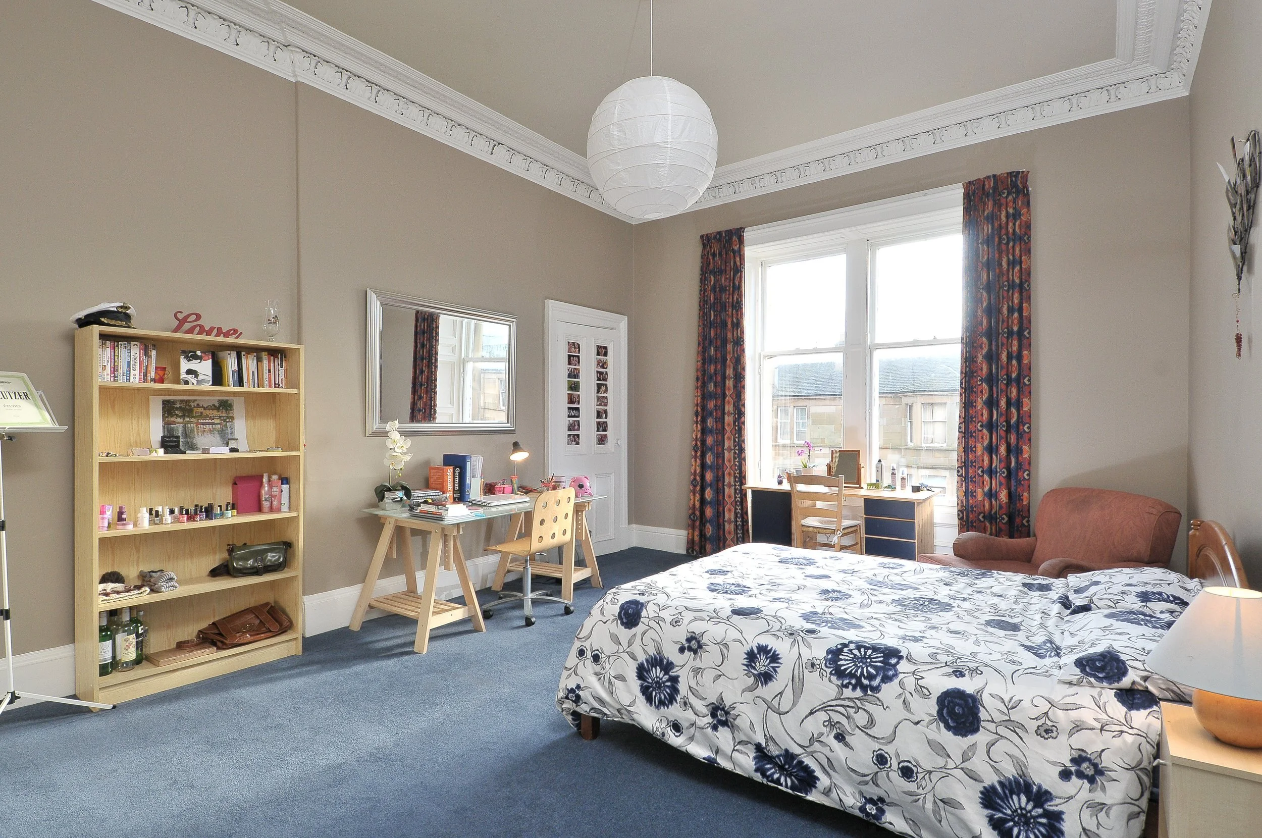 A modern wooden house with large glass windows set against a mountainous landscape, with some people visible through the window.