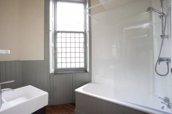Bathroom with a bathtub, shower, sink, and a window with grid pattern bars.