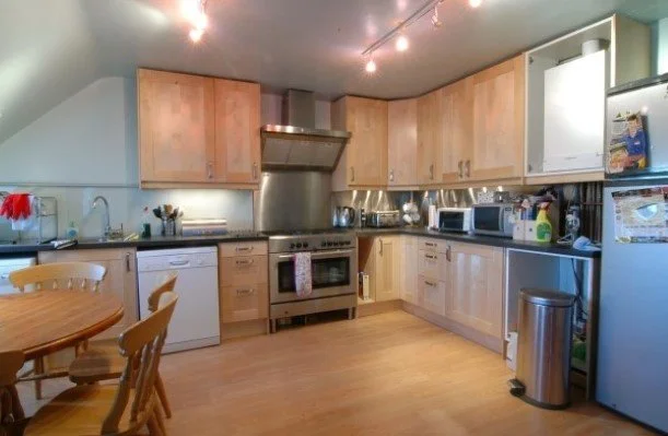 Kitchen with wooden cabinets, stainless steel appliances, including a range, microwave, and refrigerator, and a small dining table with chairs.