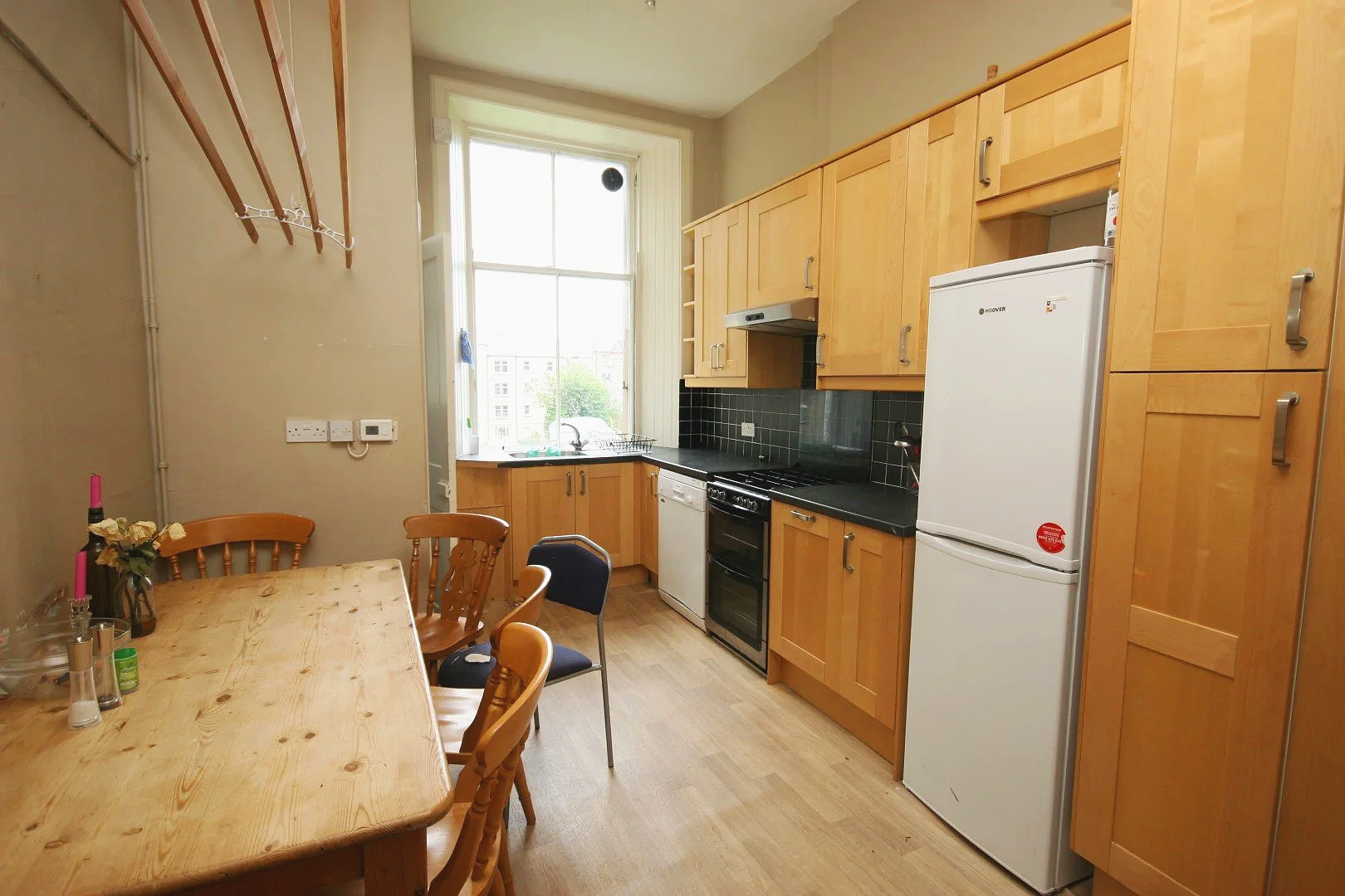 Kitchen with wooden cabinets, a window above the sink, a black stovetop, a white refrigerator, and a wooden dining table with chairs.
