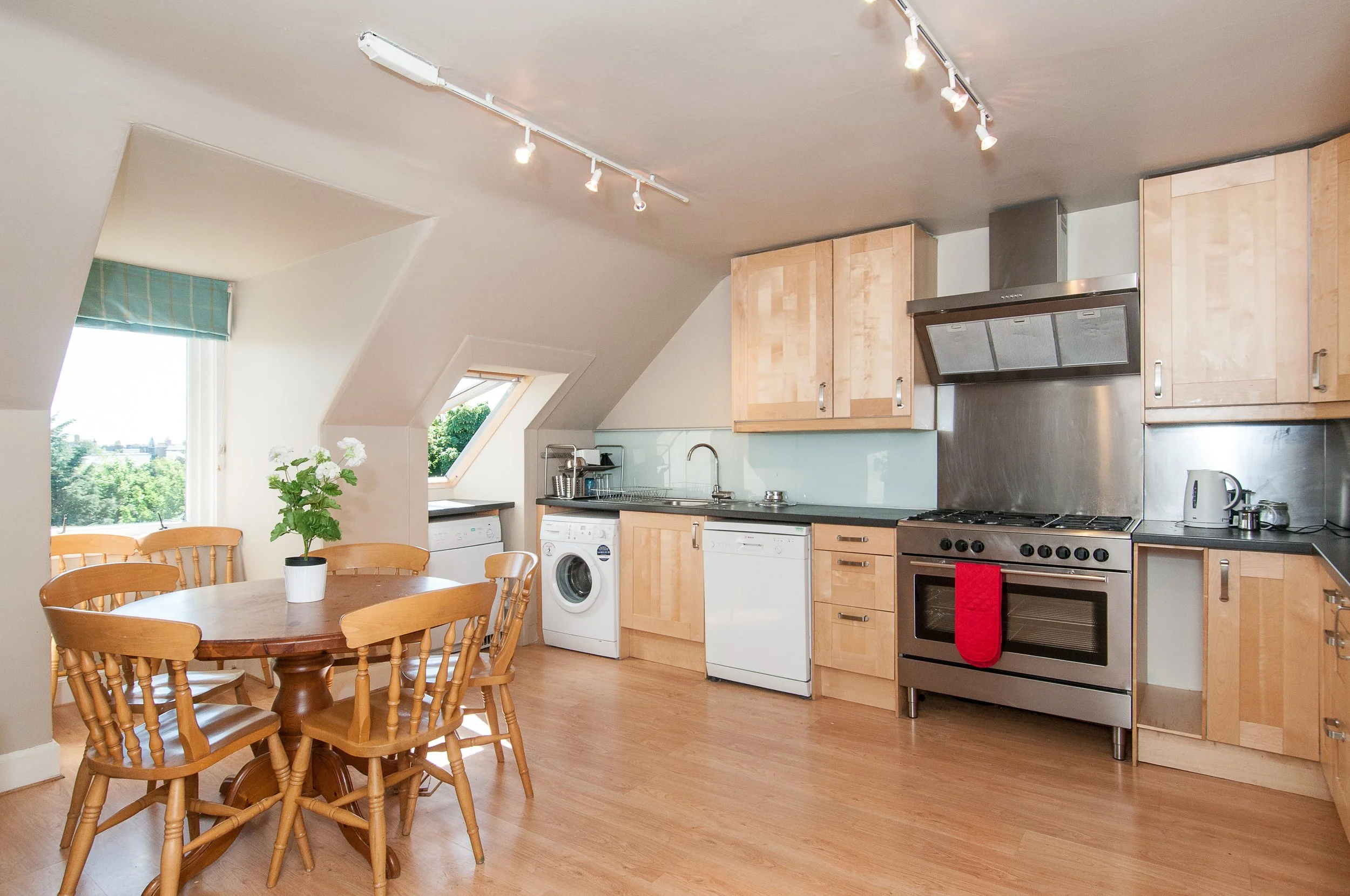 A modern wooden house with large glass windows set against a mountainous landscape, with some people visible through the window.