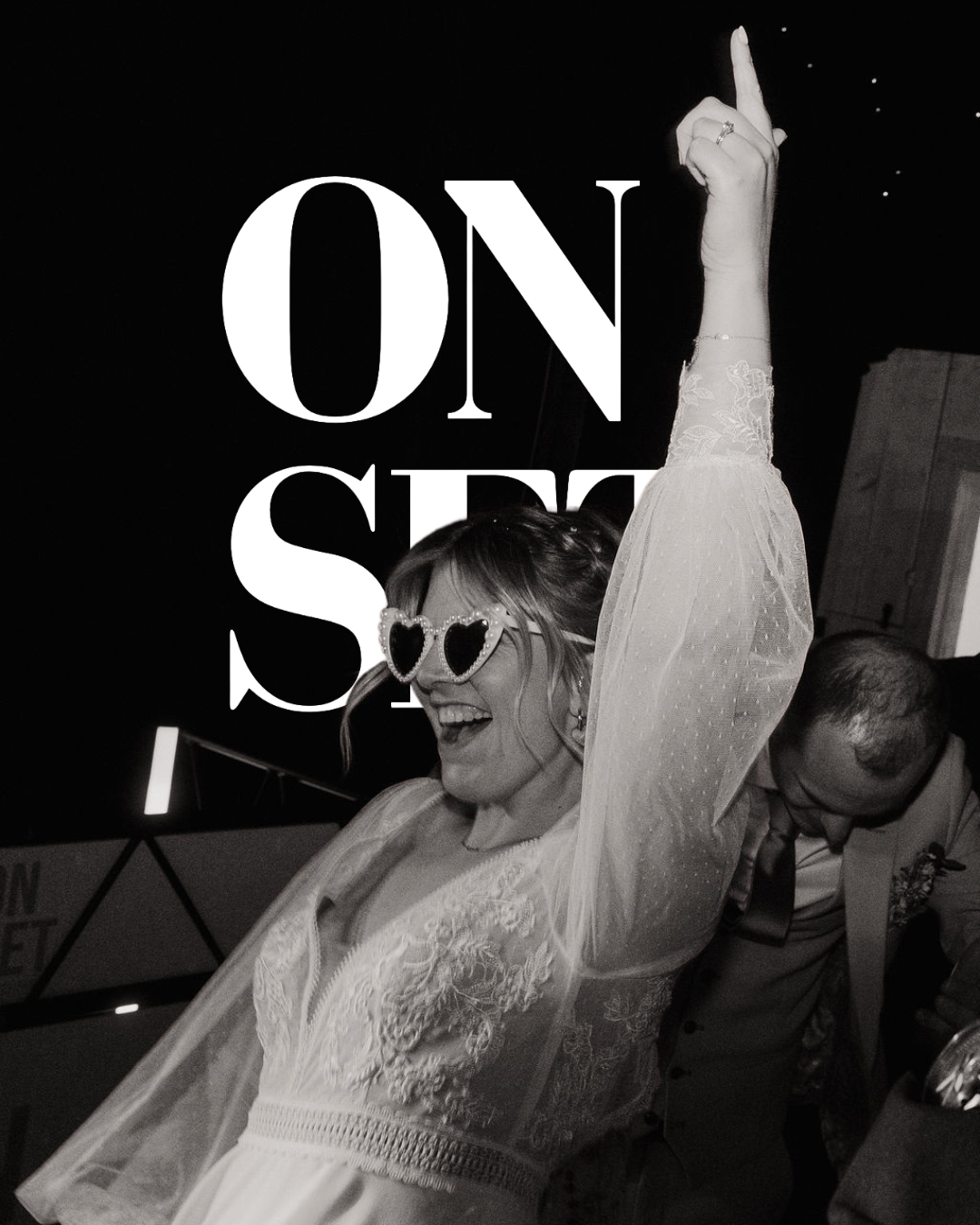 A woman wearing heart-shaped sunglasses, smiling and dancing with her arm raised, at a party or celebration.