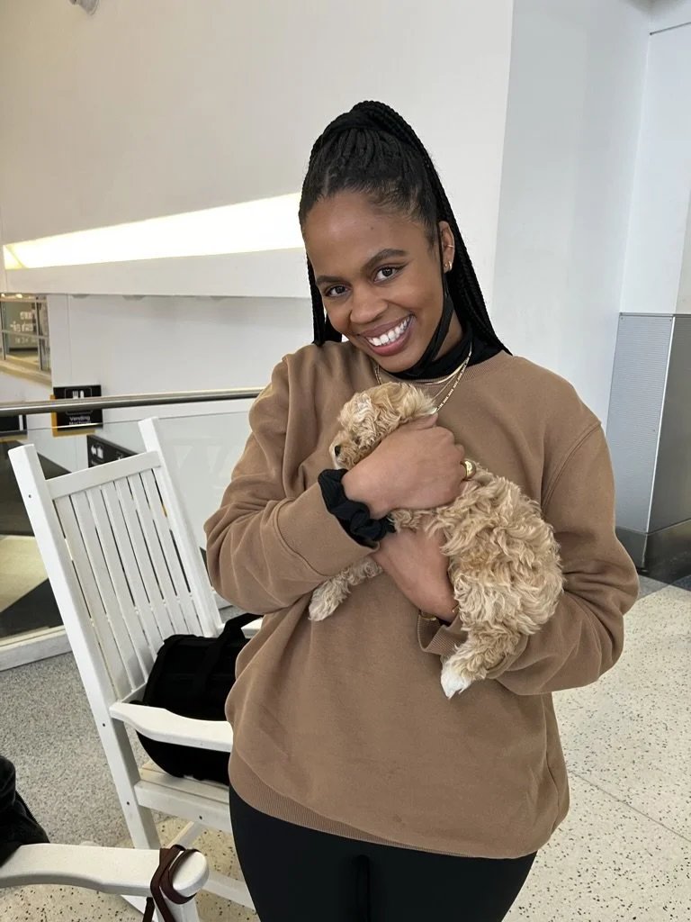 A woman smiling and holding a small, curly-haired puppy in an indoor setting.