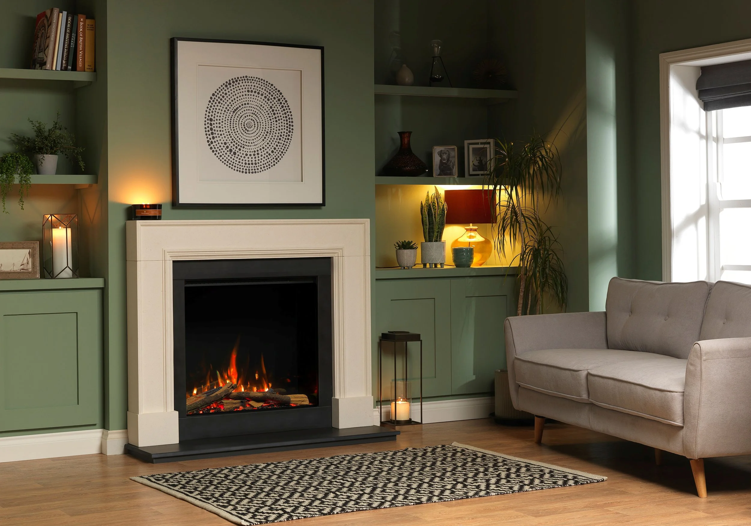 Living room with gas fireplace, beige sofa, green walls, built-in shelves with books and decor, candles, and potted plants near window.
