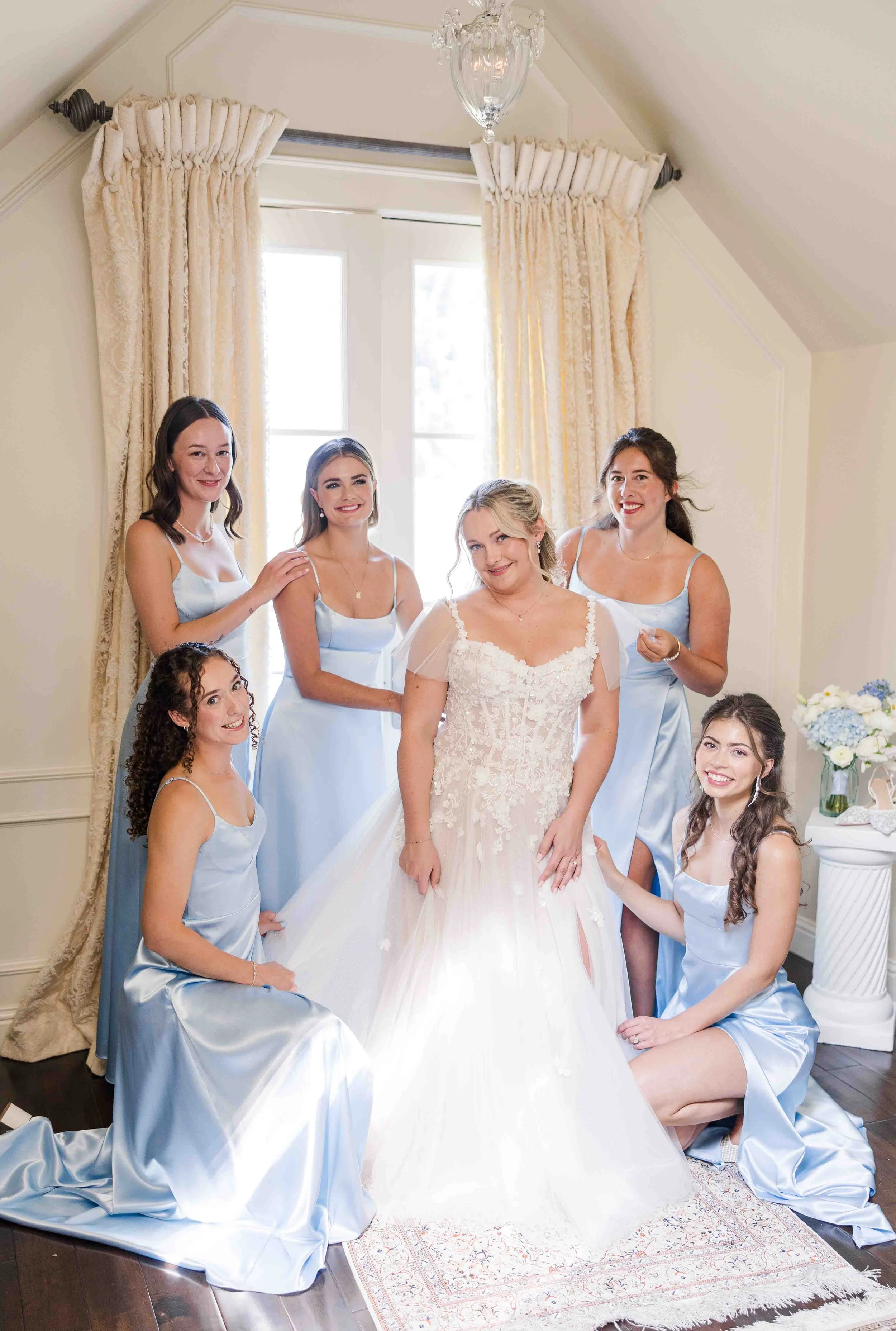 La mariée pose au centre de ses demoiselles d'honneur vêtues de magnifiques robes longues en satin bleu pastel dans une suite nuptiale.