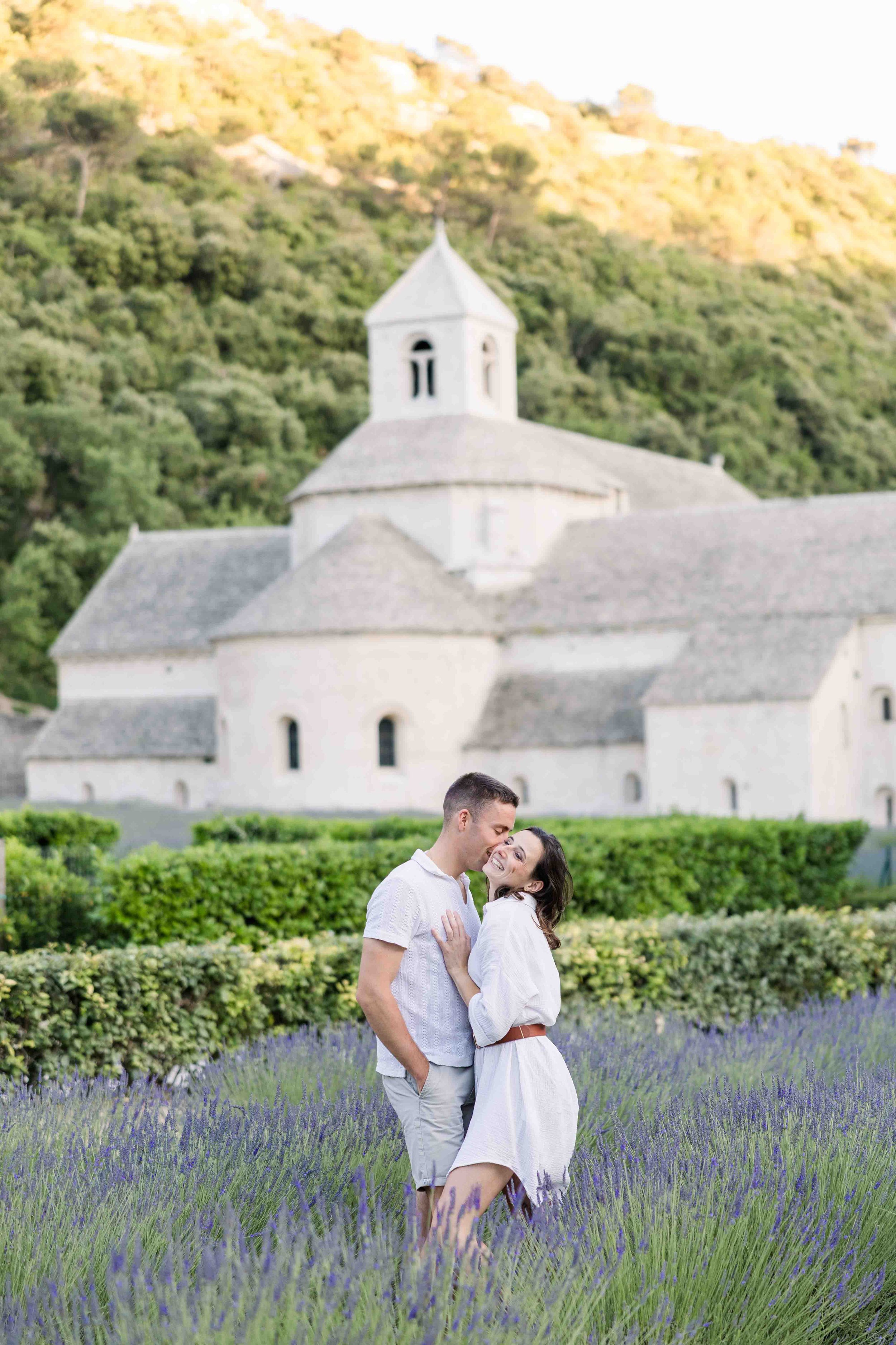 Séance photo d'engagement au cœur des lavandes en fleurs, avec la façade emblématique de l'Abbaye Notre-Dame de Sénanque.