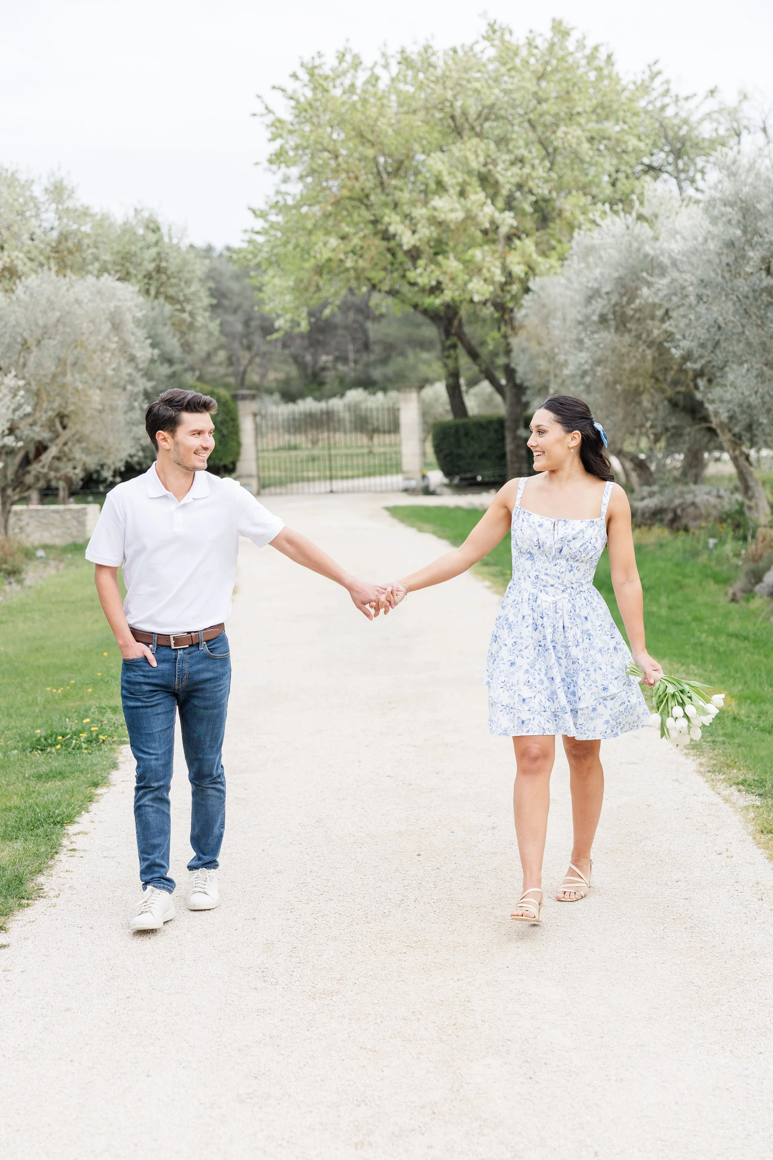 Le couple marche main dans la main, s'éloignant le long d'une allée de gravier bordée de cyprès et de haies formelles au Mas de La Rose.