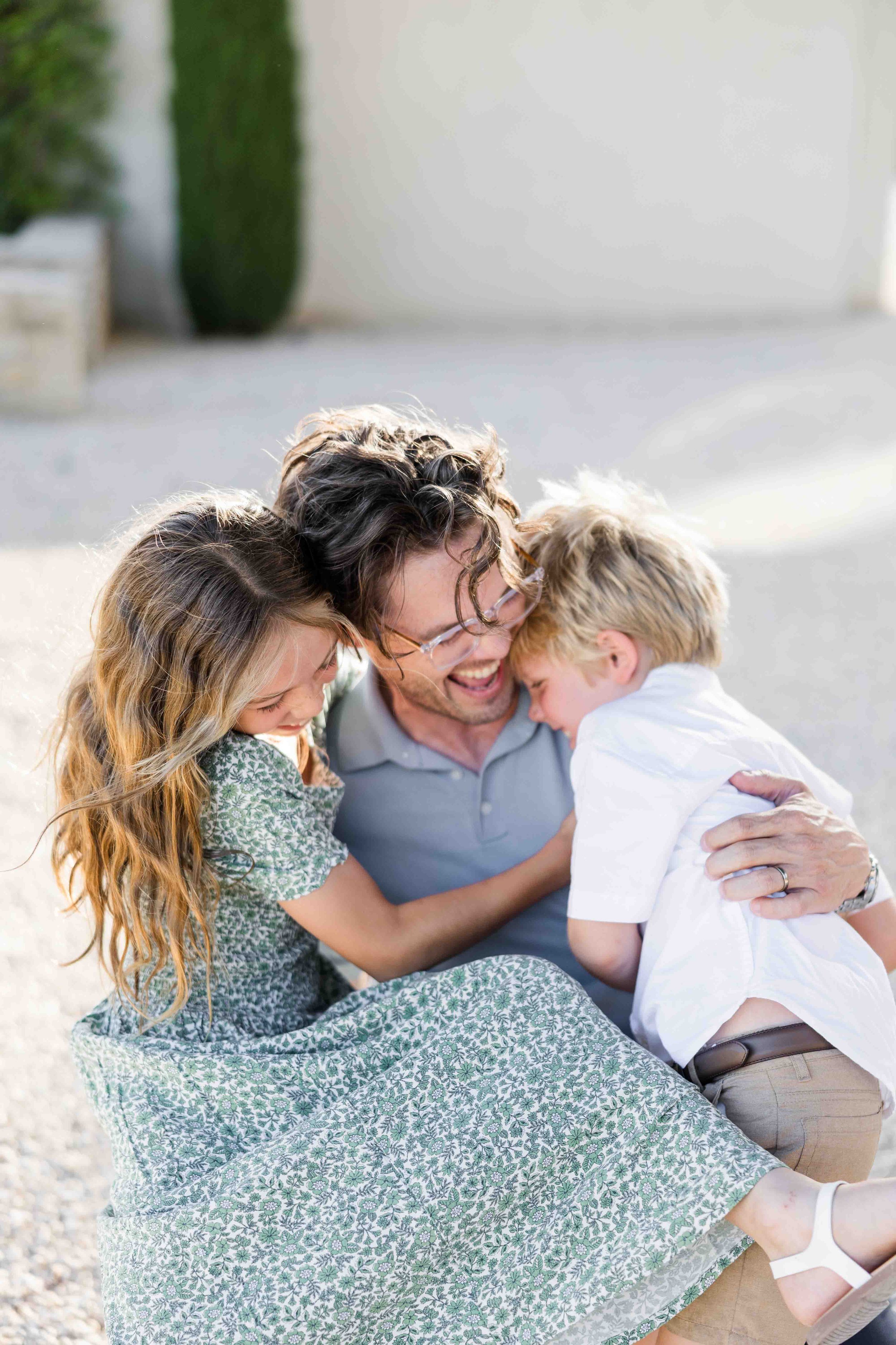 Photo de famille chaleureuse montrant les parents assis par terre et entourés de leurs enfants qui les calinent dans une cour ensoleillée.