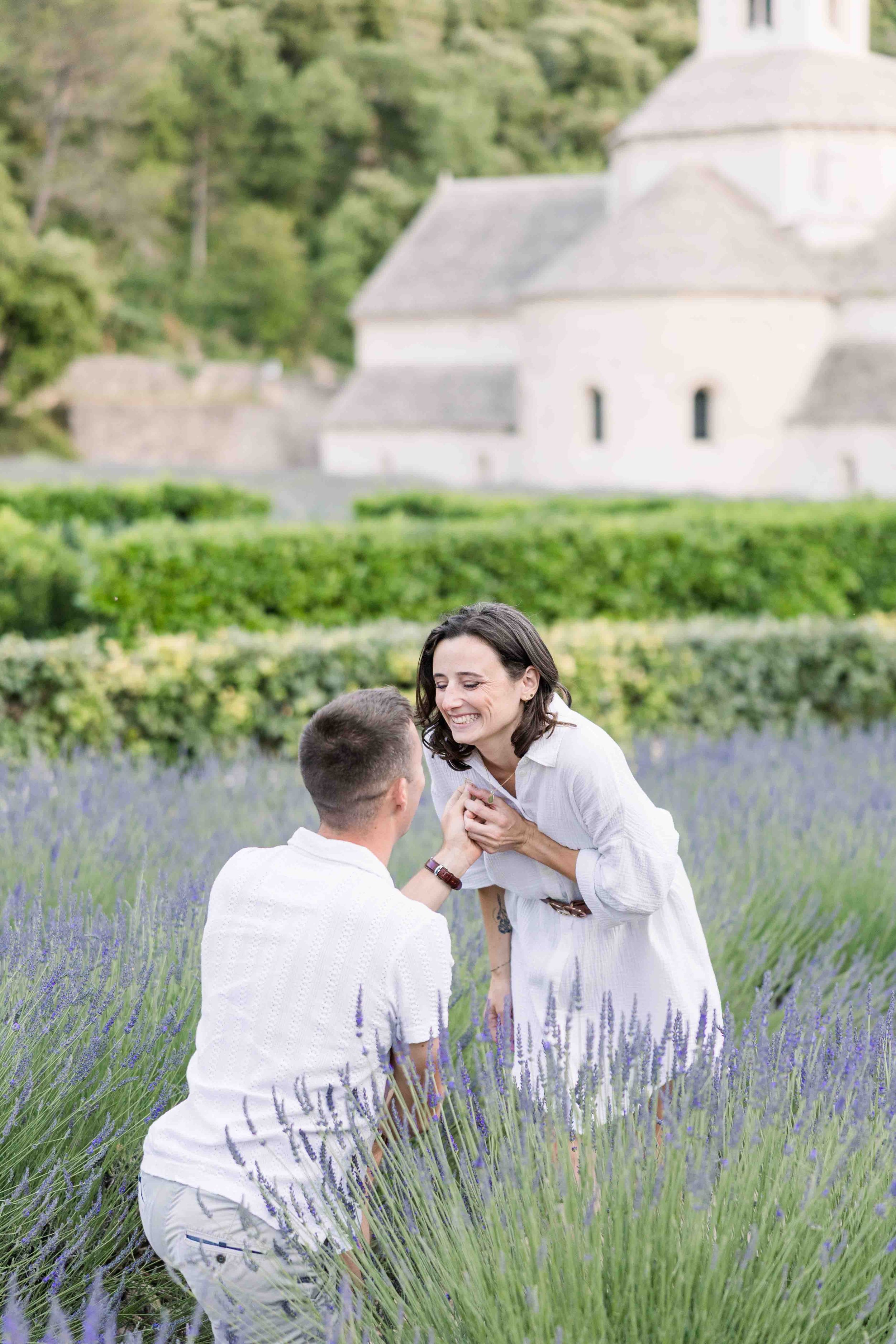 Demande en mariage romantique dans les champs de lavande de l'Abbaye de Sénanque à Gordes, moment complice entre les futurs mariés.