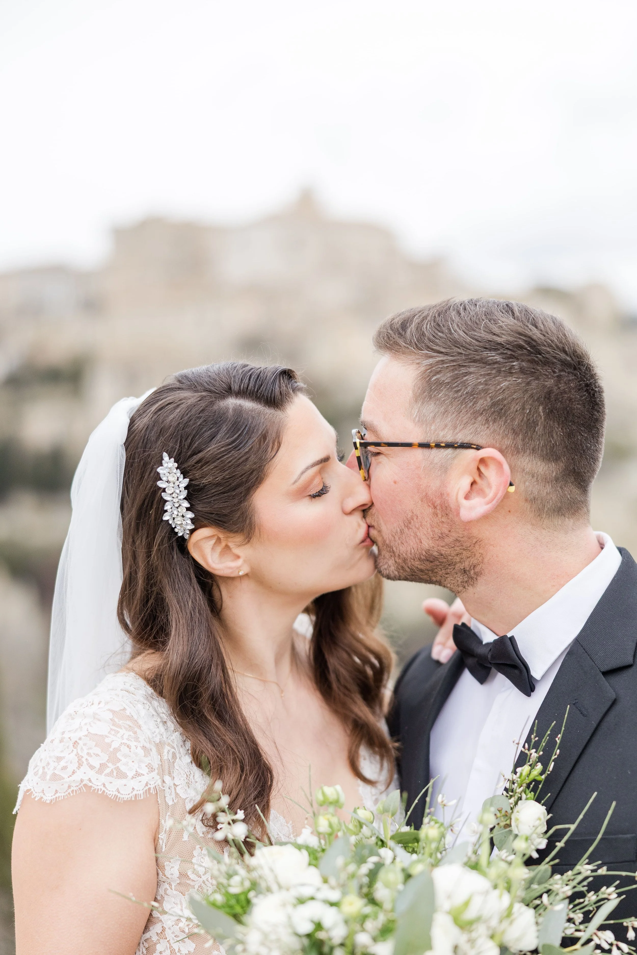 Portrait rapproché romantique des mariés s'embrassant tendrement avec le bouquet de fleurs blanches et eucalyptus au premier plan.