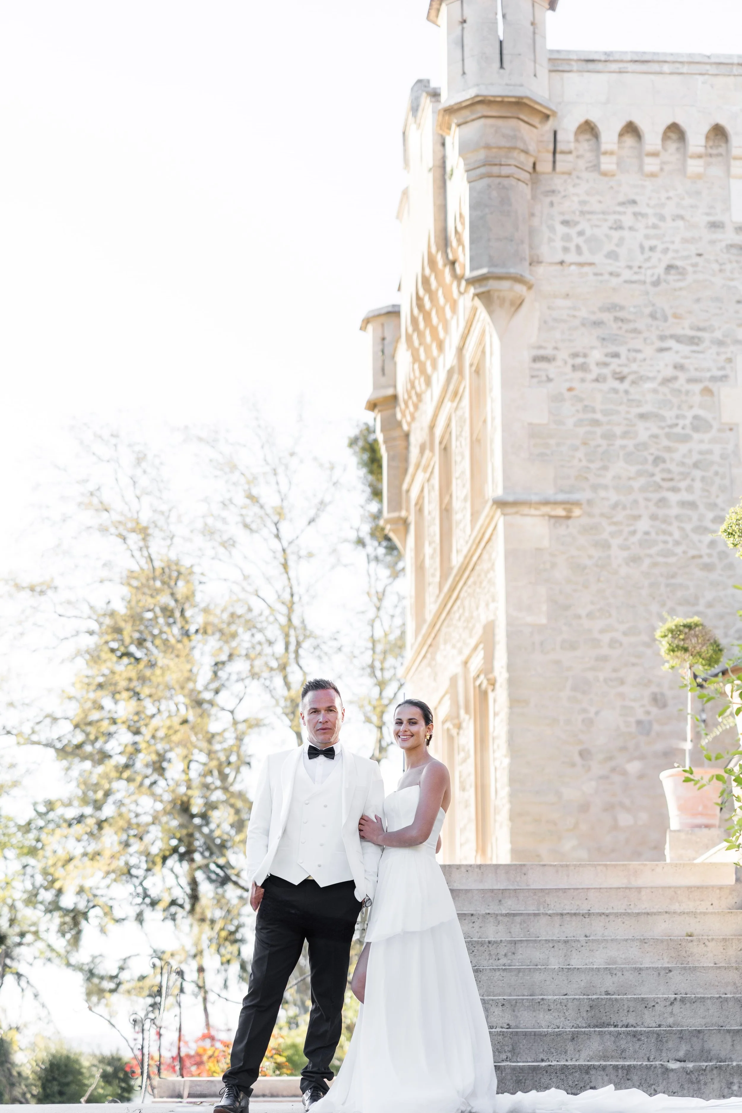 Portrait plein pied des mariés posant devant l'escalier en pierre d'un château majestueux en Provence.