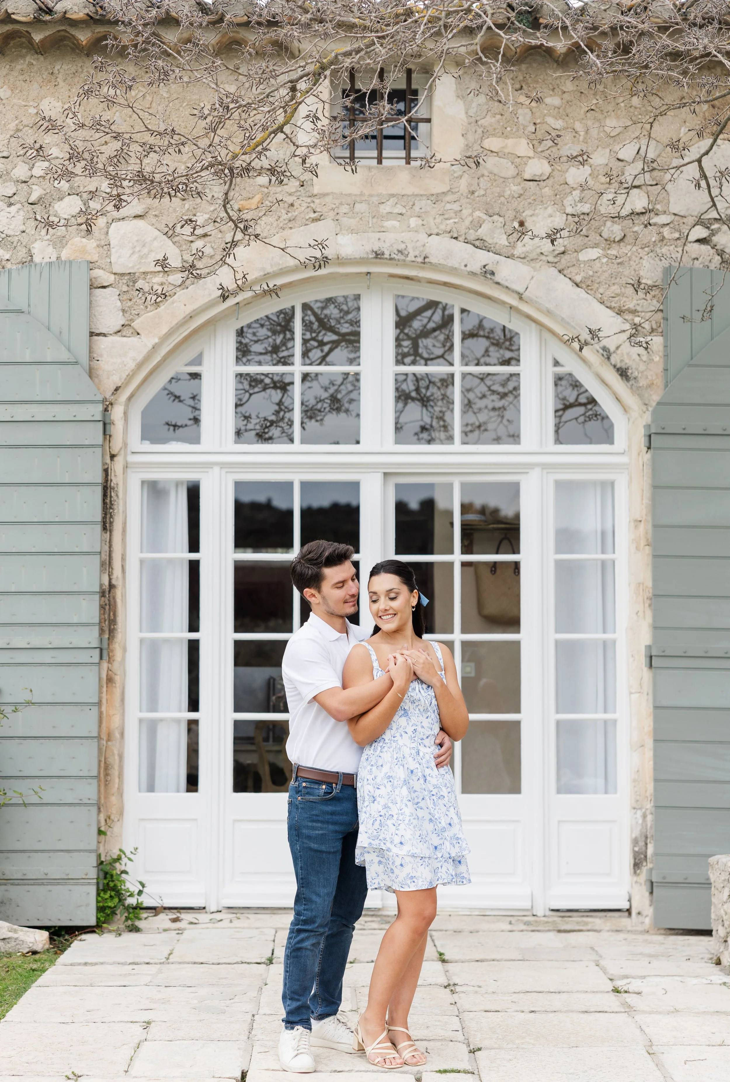 Le couple se tient devant la magnifique bastide provençale en pierre du Mas de La Rose à Orgon, entouré d'un parc arboré et d'oliviers.