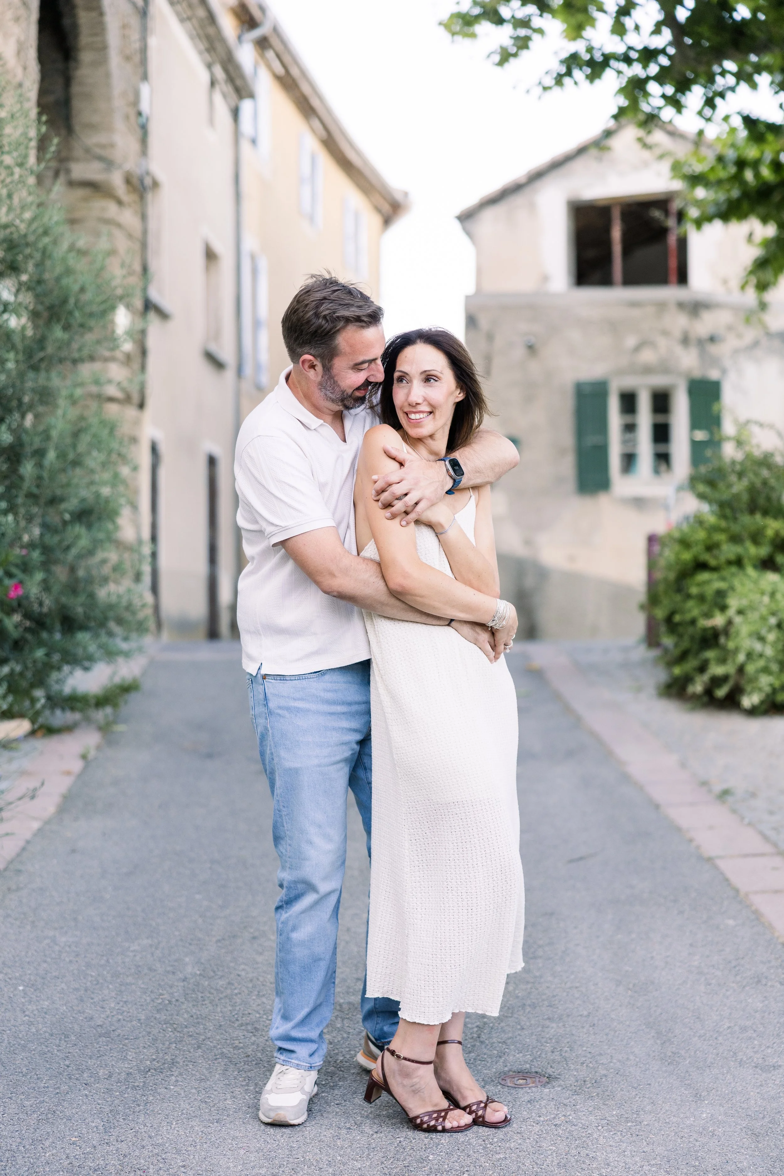 Un couple s'enlace tendrement dans une ruelle de village provençal, partageant un moment intime et complice.
