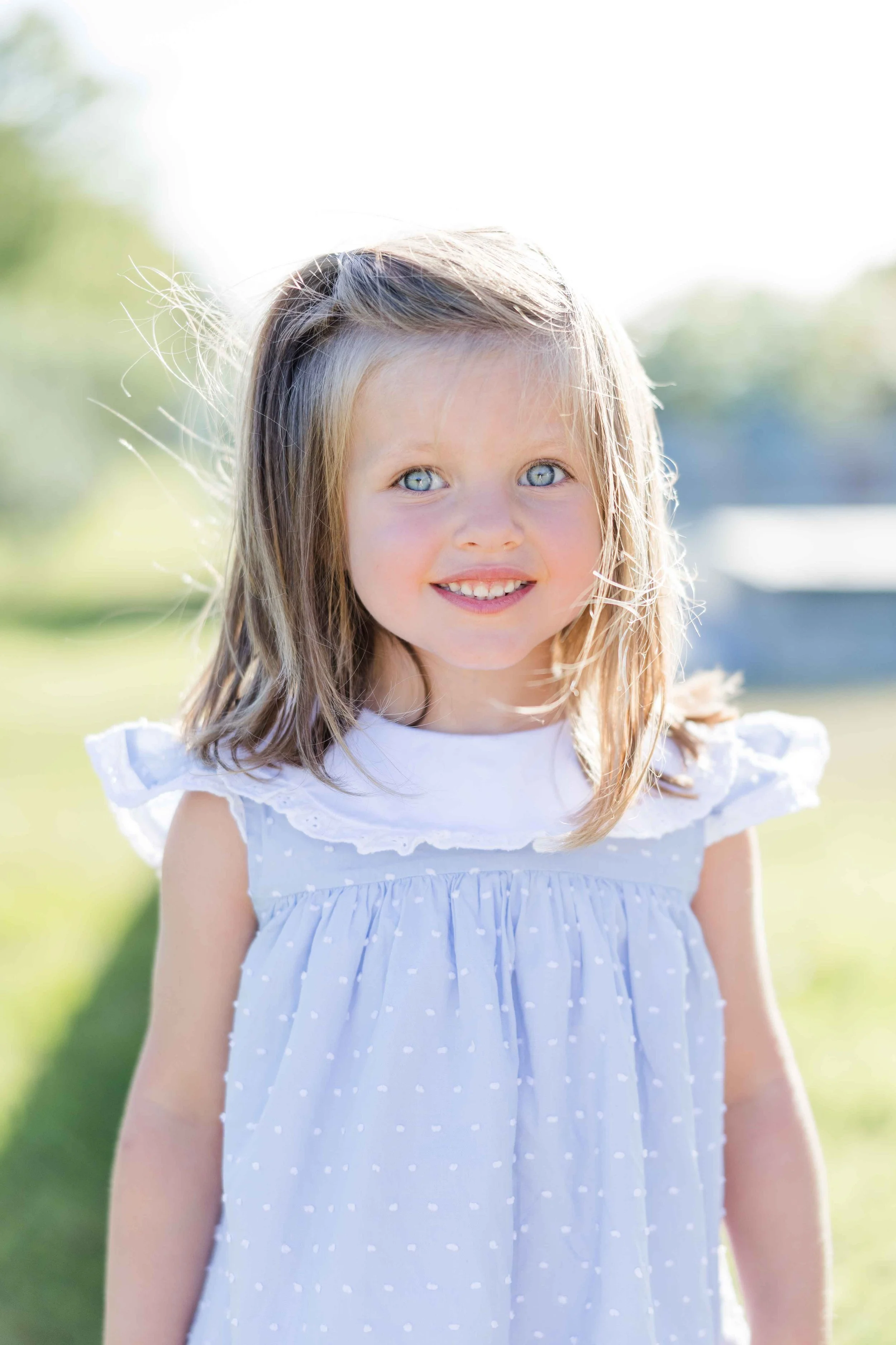 Portrait en lumière naturelle d'une petite fille aux yeux bleus et cheveux blonds, vêtue d'une robe bleue à col blanc lors d'une séance photo en Provence.