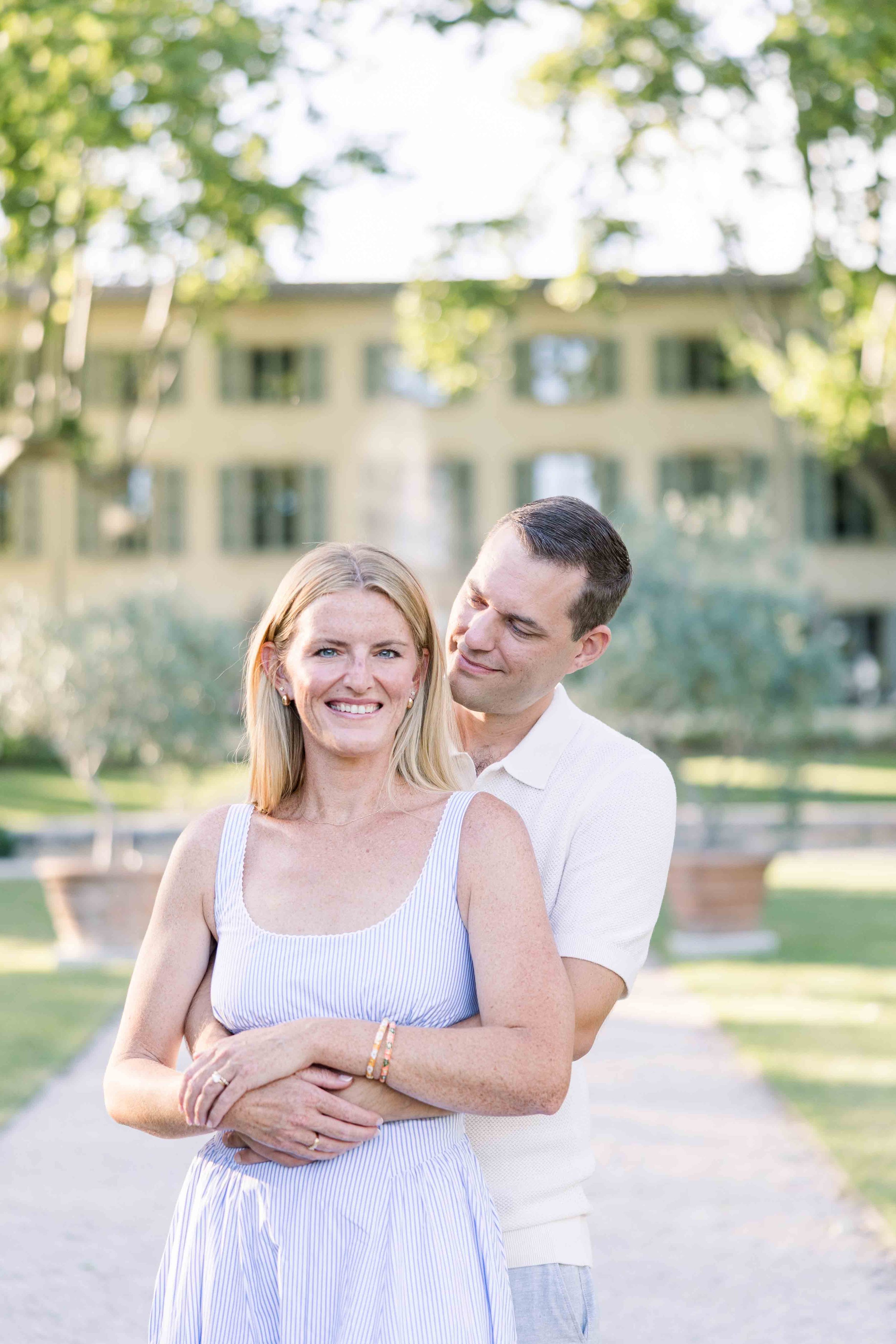Un plan moyen du couple s'embrassant sur une allée du parc devant la bastide du Domaine de Fontenille dans le Luberon.