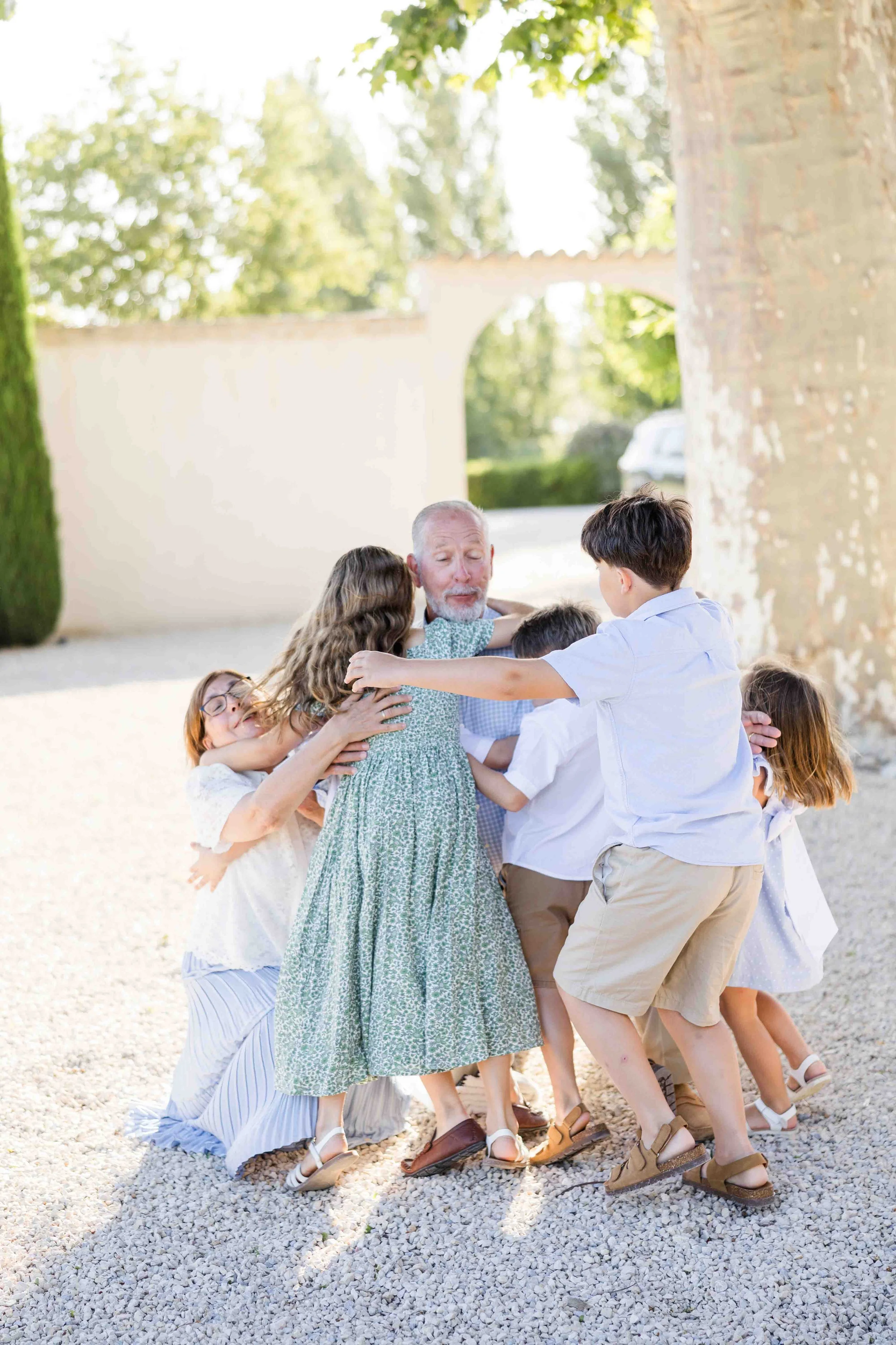 Moment spontané et joyeux d'un groupe d'enfants et cousins s'enlaçant tous ensemble en cercle dans une cour de mas provençal.