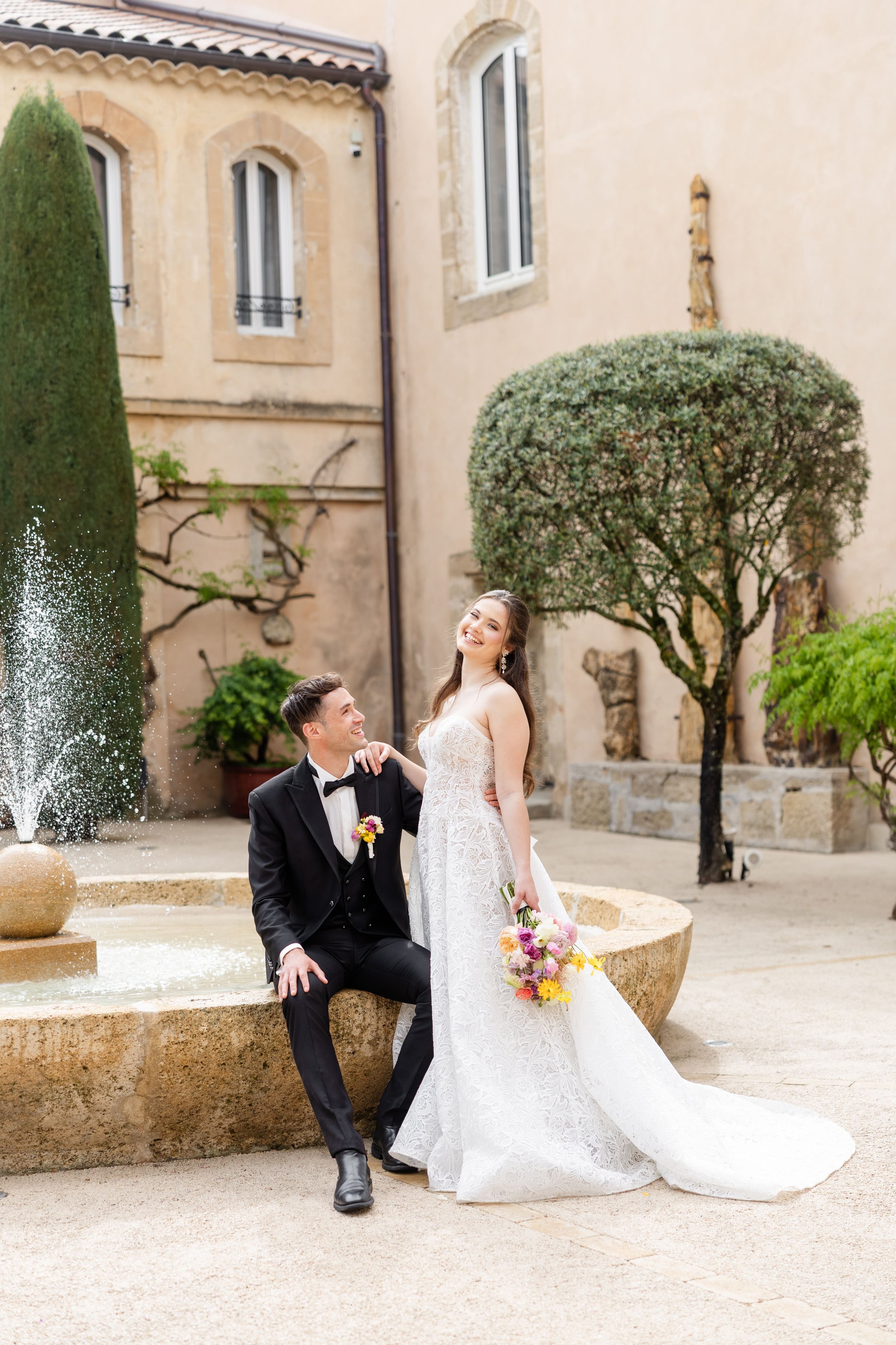 Les mariés posant avec élégance à côté d'une fontaine en pierre dans la cour intérieure d'un domaine de prestige en Provence.