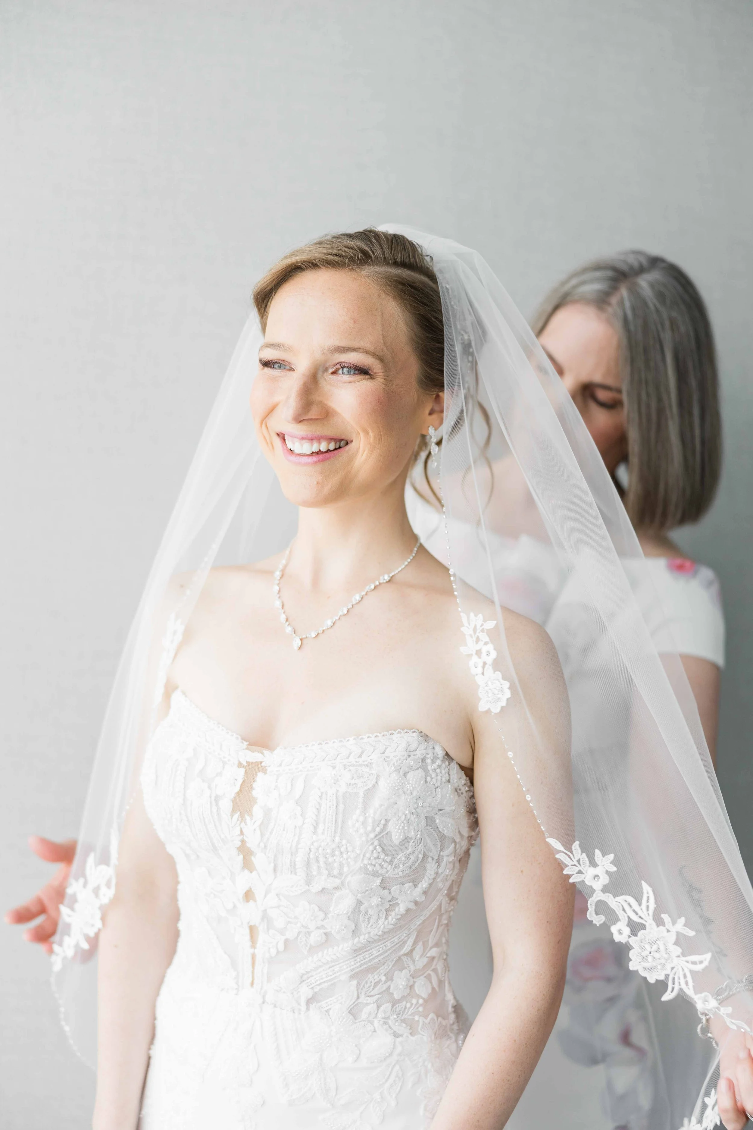 Moment plein de tendresse de la pose du voile en dentelle sur la mariée par sa mère durant la préparation.