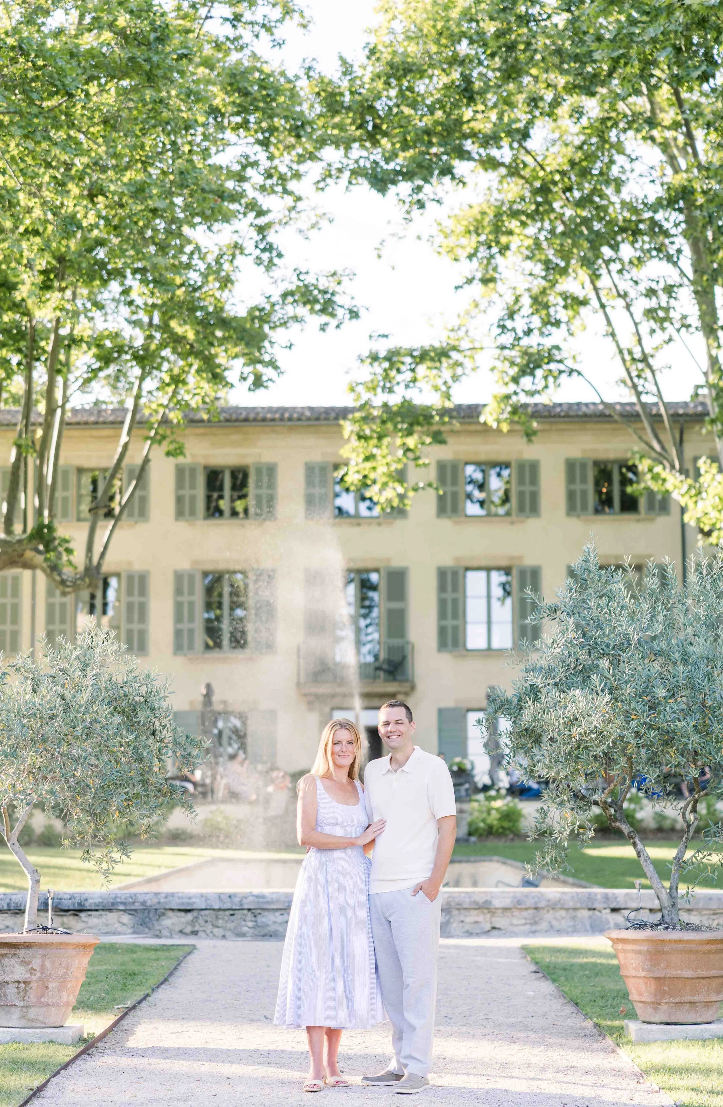 Le couple se tient devant la magnifique bastide provençale du Domaine de Fontenille, entouré d'un parc arboré et d'oliviers.