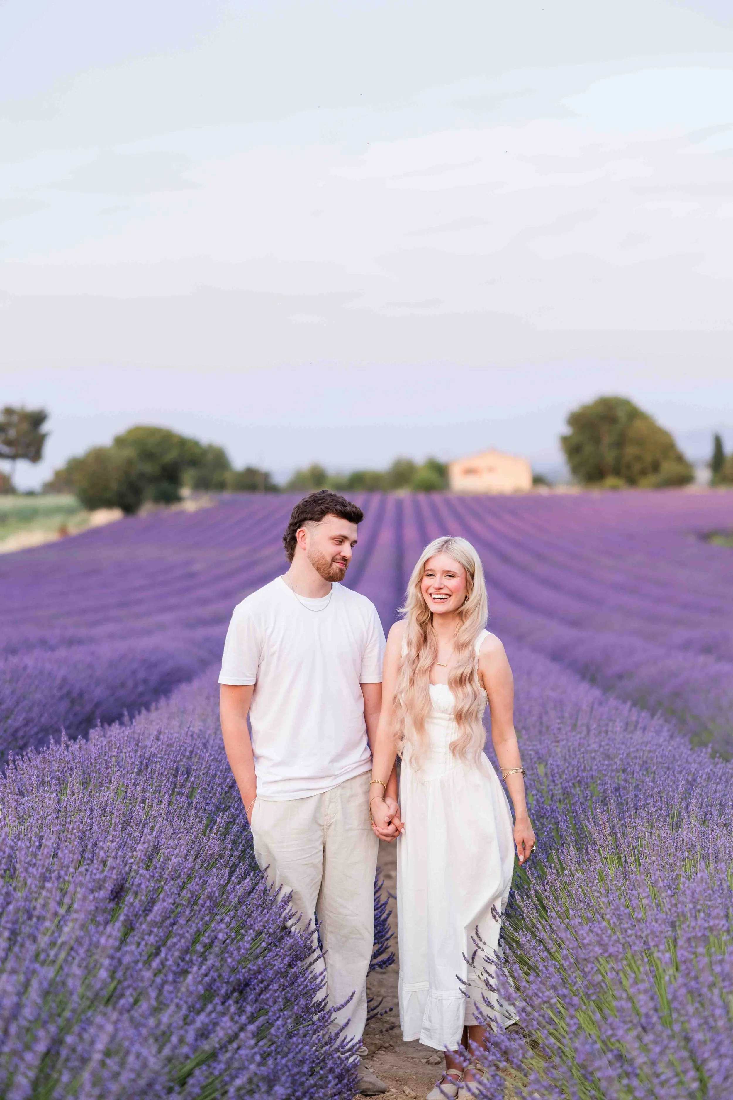 Séance photo d'engagement en Provence : couple se promenant main dans la main dans une allée de lavande fleurie