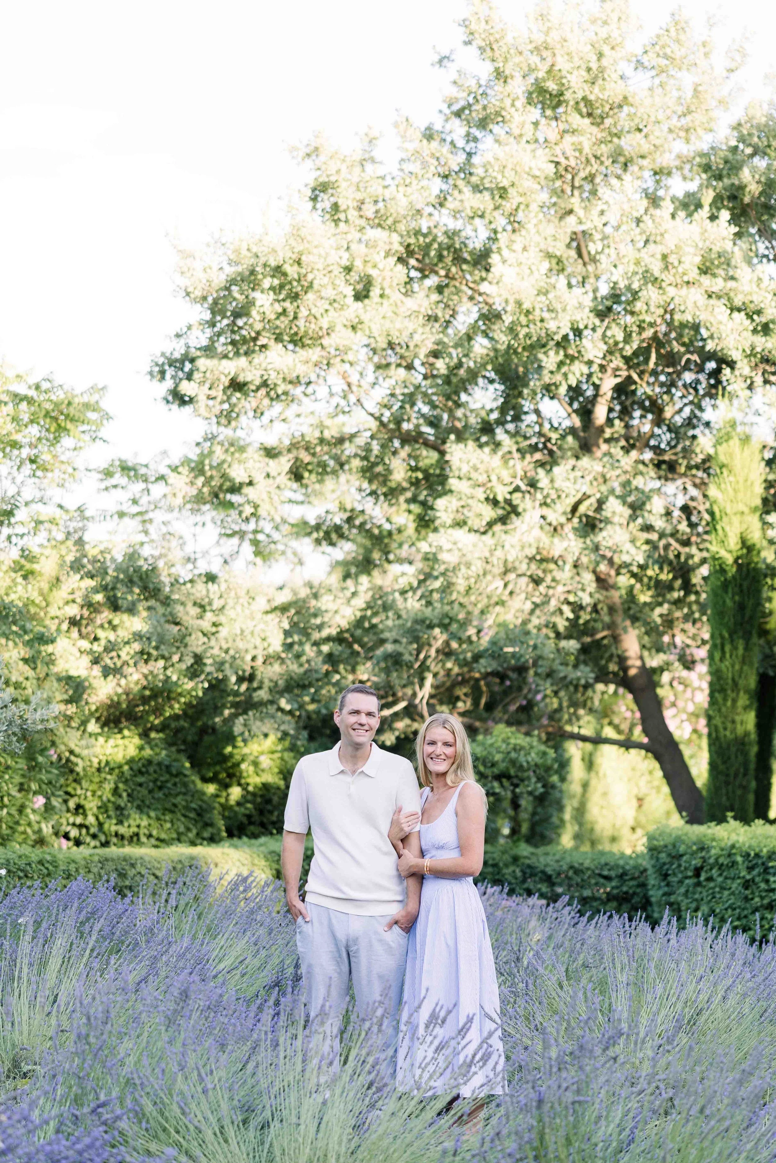 Le couple pose en souriant au milieu d'un champ de lavande en fleurs, avec les jardins du Domaine de Fontenille en arrière-plan.