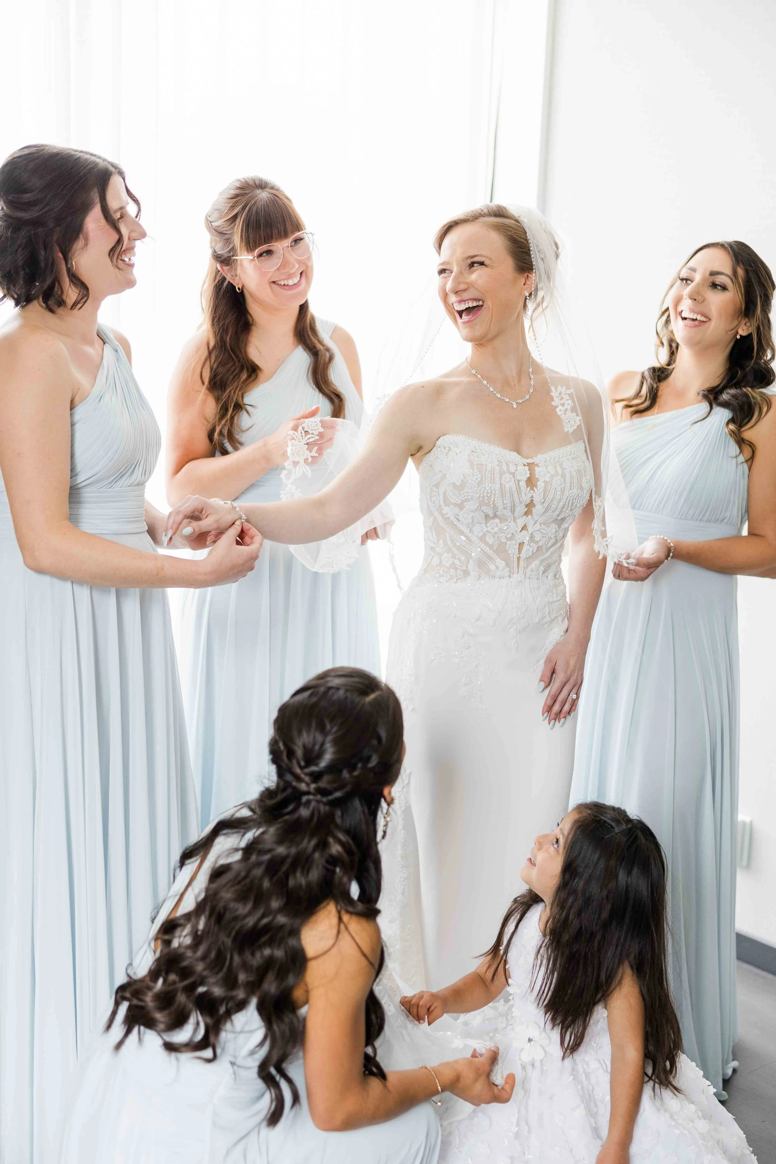 La mariée riant avec ses demoiselles d'honneur et deux petites filles vêtues de robes bleu ciel lors des préparatifs du mariage.