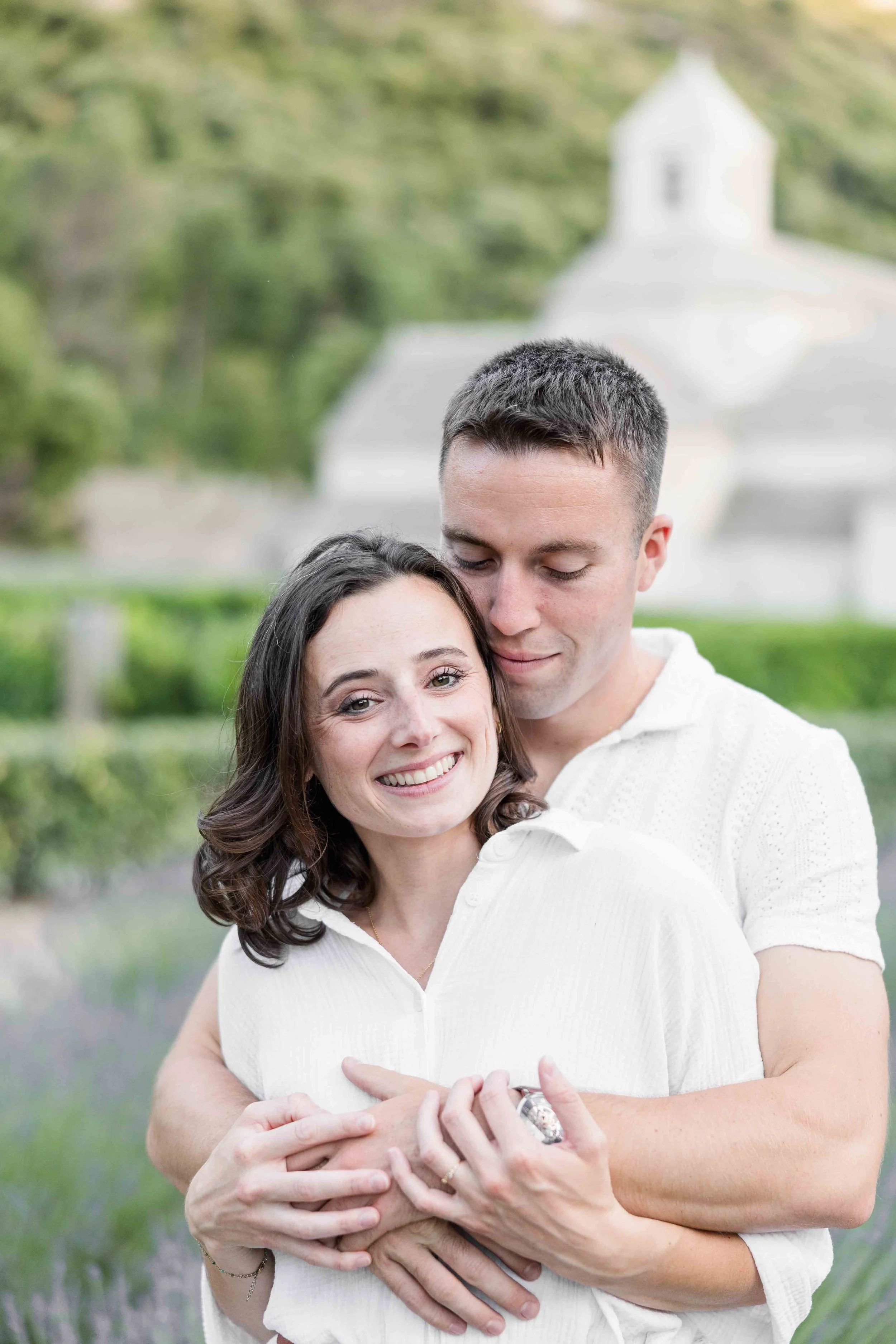 Portrait rapproché d'un couple enlacé en tenues blanches, souriant devant l'Abbaye Notre-Dame de Sénanque à Gordes en Provence.