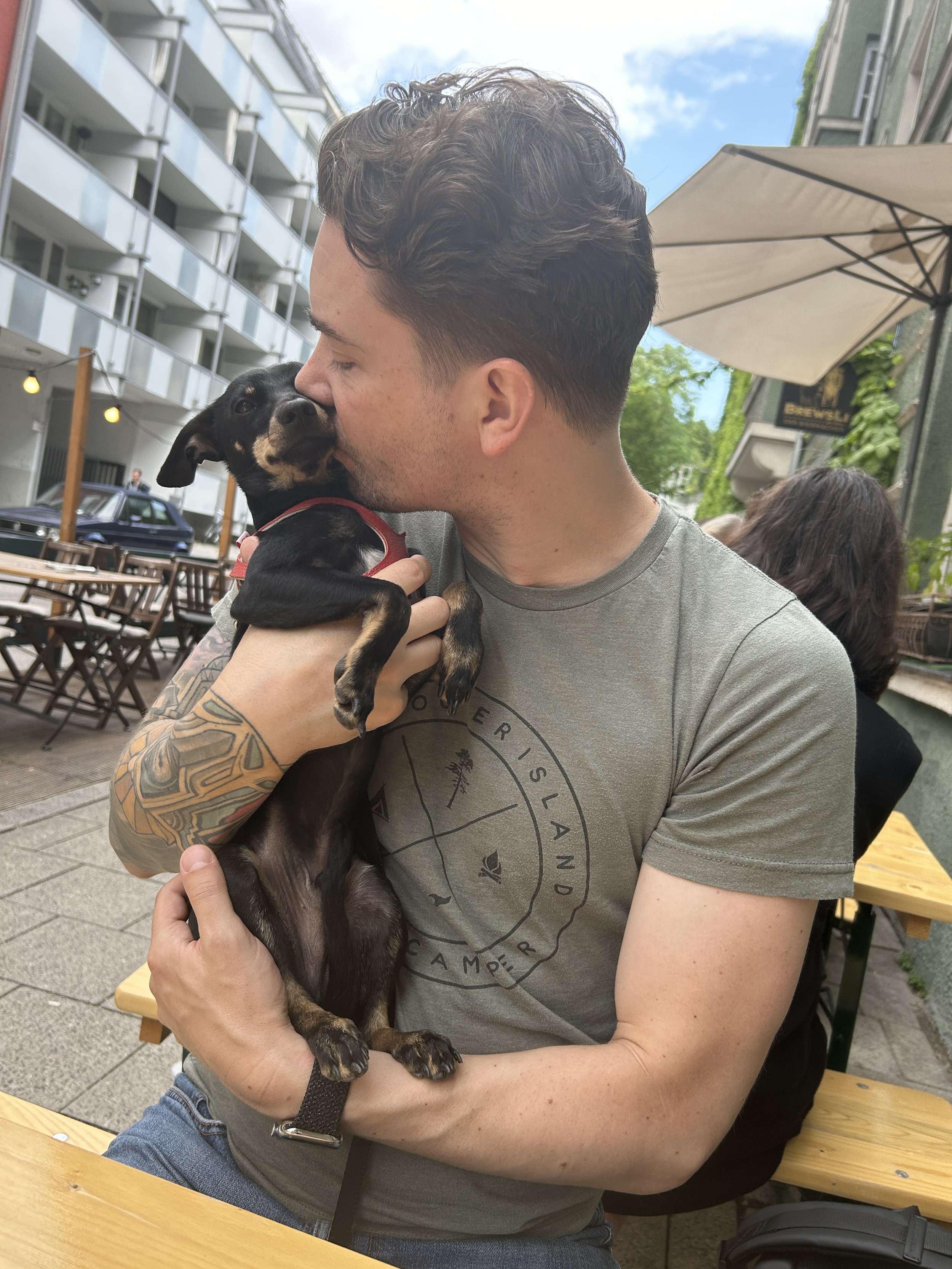 Kadoga founder Aaron holding his small dog Gus at an outdoor café in Munich.