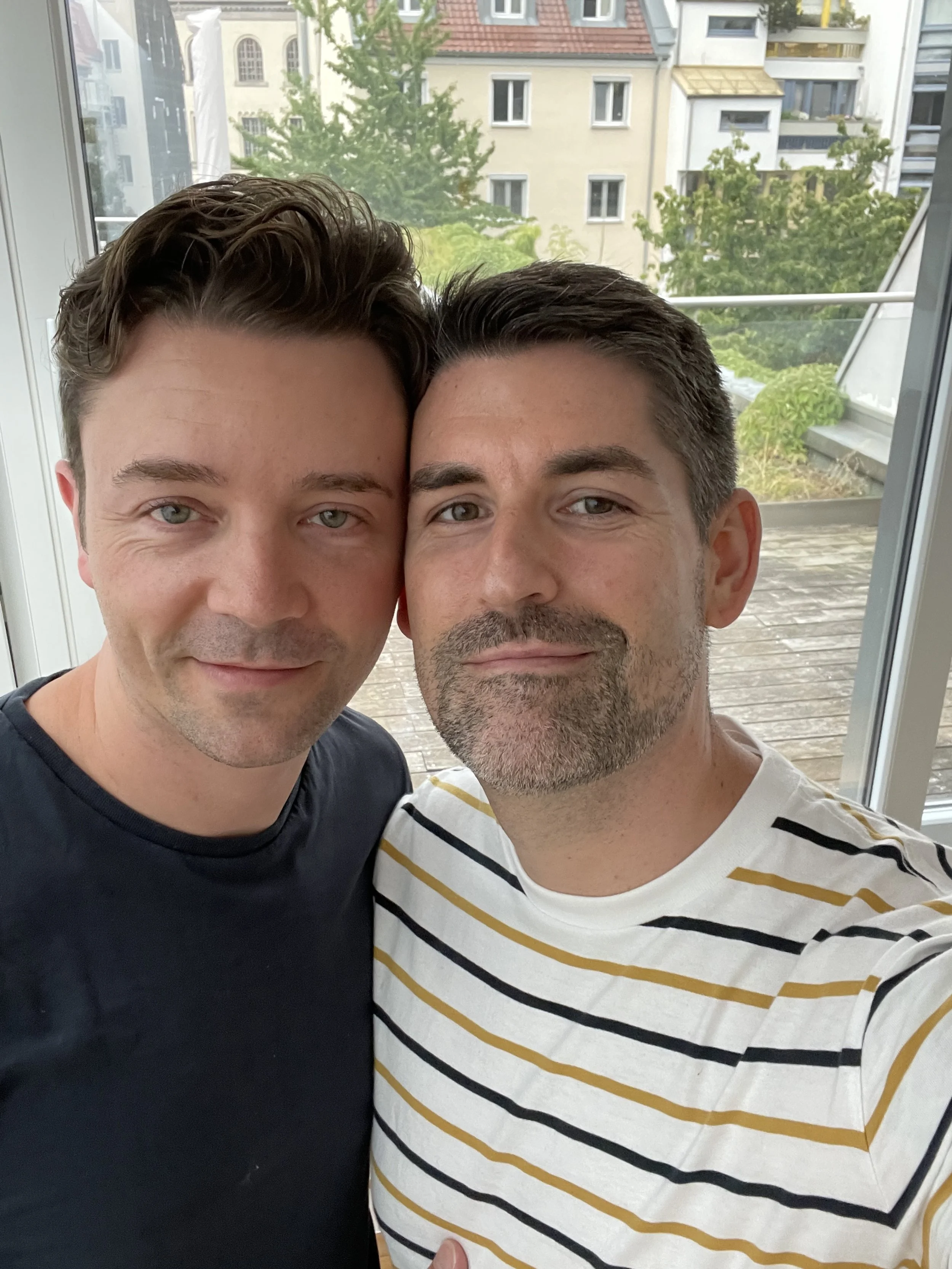 Zwei Männer lächeln gemeinsam vor dem Hintergrund von Gebäuden.