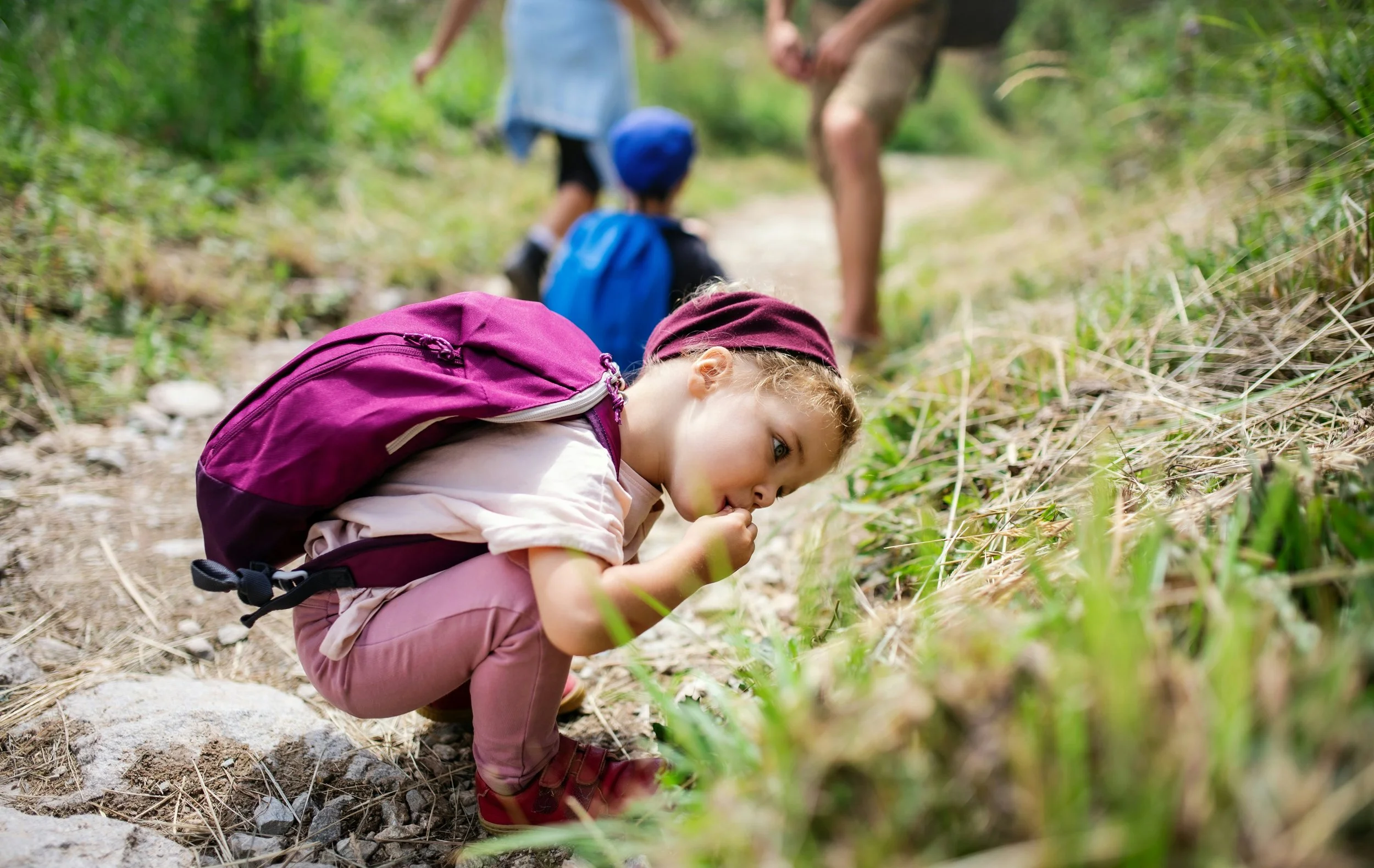 Photo de Getty Images sur Unsplash. Une fille observe des herbes, peut-être quelques insectes. Elle porte un sac-à-dos et un bandana violets. Elle est accroupie, absorbée par ce qu'elle observe. Elle s'est arrêtée de marcher pour observer la nature.