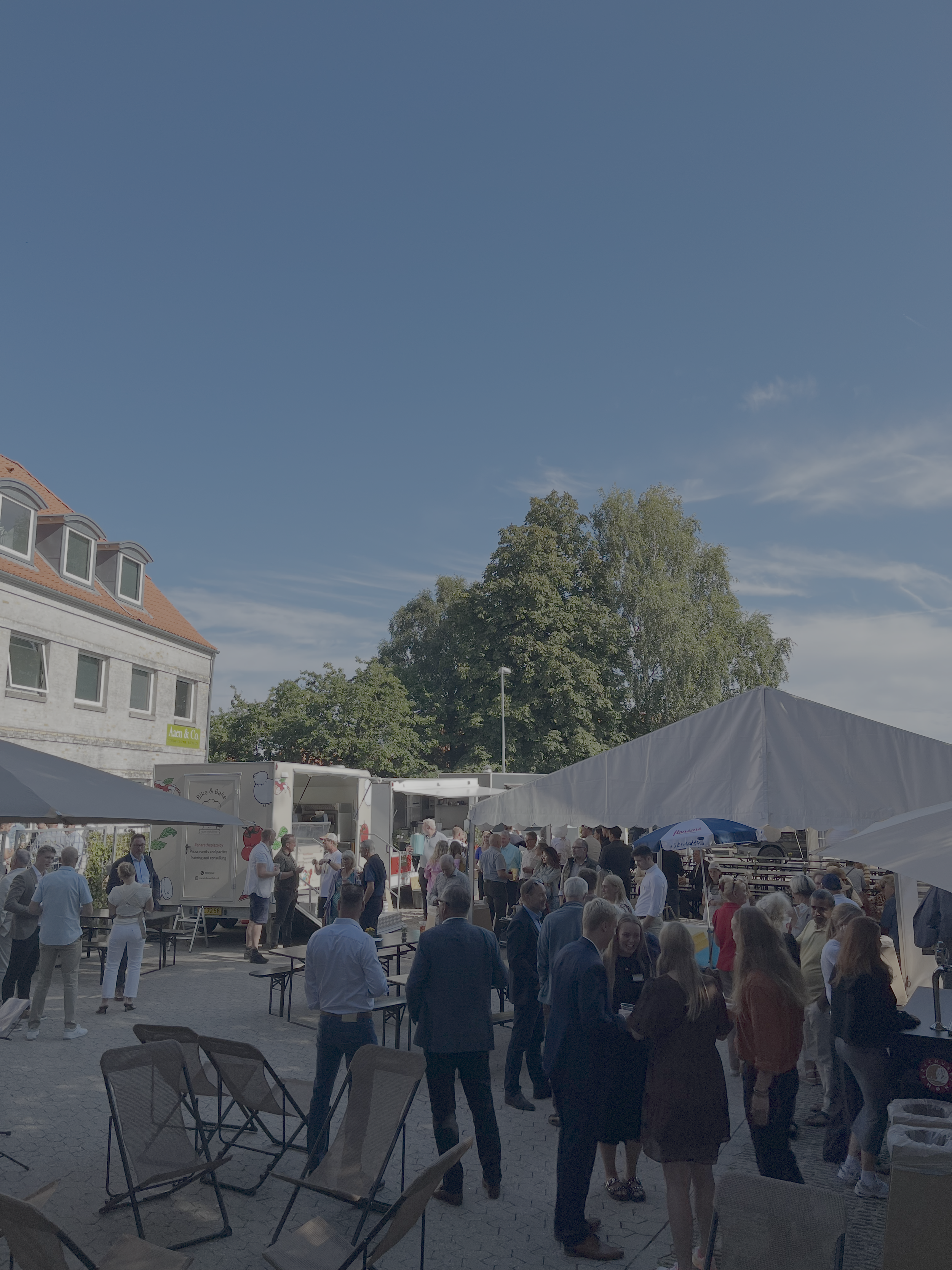 Sommerarrangement i Aarhus med mange mennesker samlet under telte og foodtrucks i solskin. Netværksevent i bymiljø med blå himmel, hyggelig stemning og lokale virksomheder.