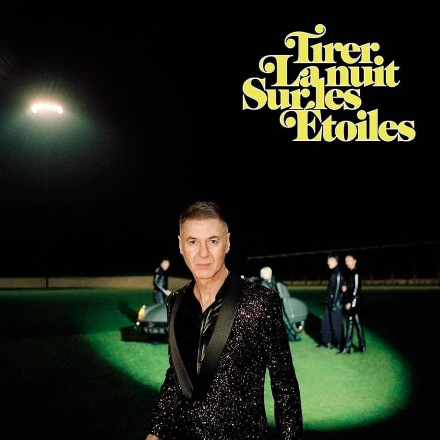 Une personne habillée d'une veste noire brillante se tient dans un espace sombre, avec des personnes et des voitures en arrière-plan, et le texte en haut à droite "Tirer la nuit sur les étoiles".