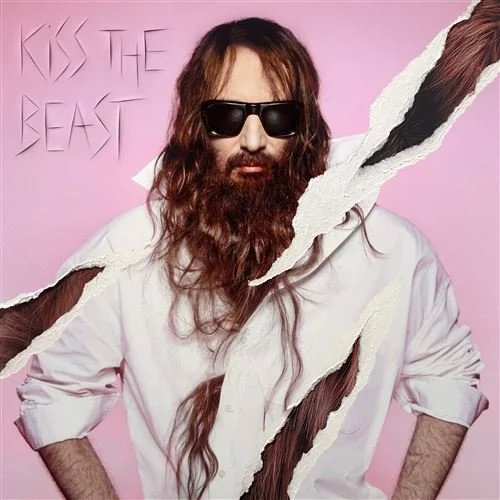 Un homme avec une longue barbe, porte des lunettes de soleil noires, vêtu d'une chemise blanche, sur un fond rose, avec des morceaux déchirés dans l'image et le texte "Kiss the Beast" en arrière-plan.