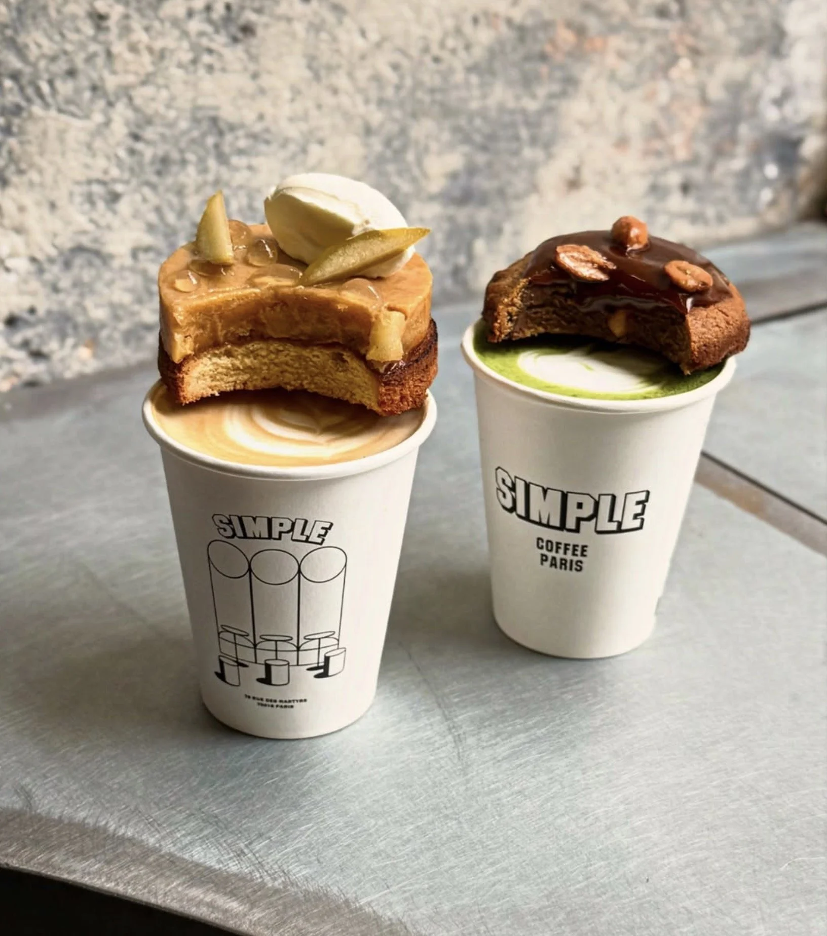 Deux cups de café avec des biscuits recouverts de caramel, chocolat et noix sur le dessus.