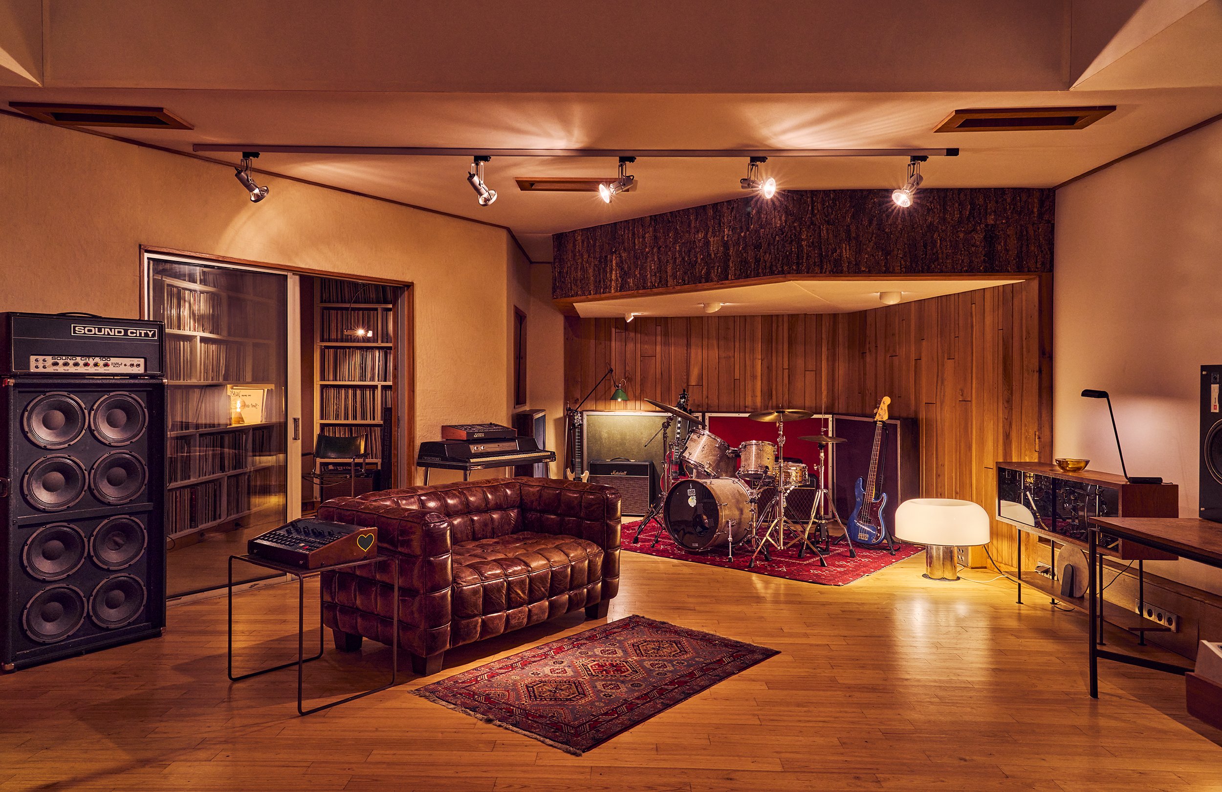 Une salle de studio d'enregistrement avec instruments de musique vintage, amplificateurs, un canapé en cuir marron et un tapis. L'espace est décoré avec du bois et une ambiance chaleureuse. Vintage. Paris.