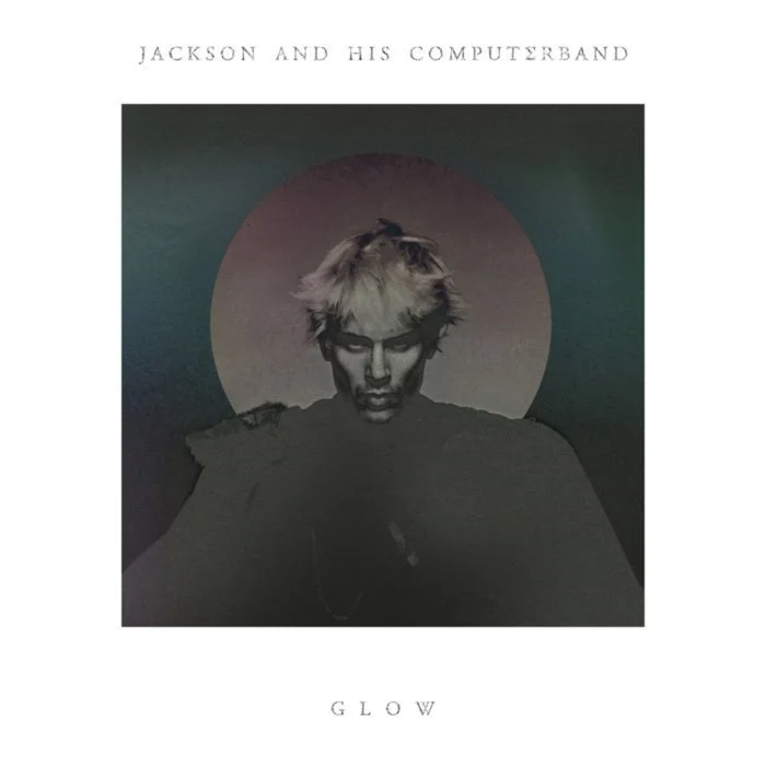 Une image en noir et blanc d'un jeune homme avec des cheveux blonds, regardant vers le bas, avec un cercle lumineux derrière sa tête. En haut, il y a le texte "Jackson and His Computerband" et en bas, le mot "Glow".