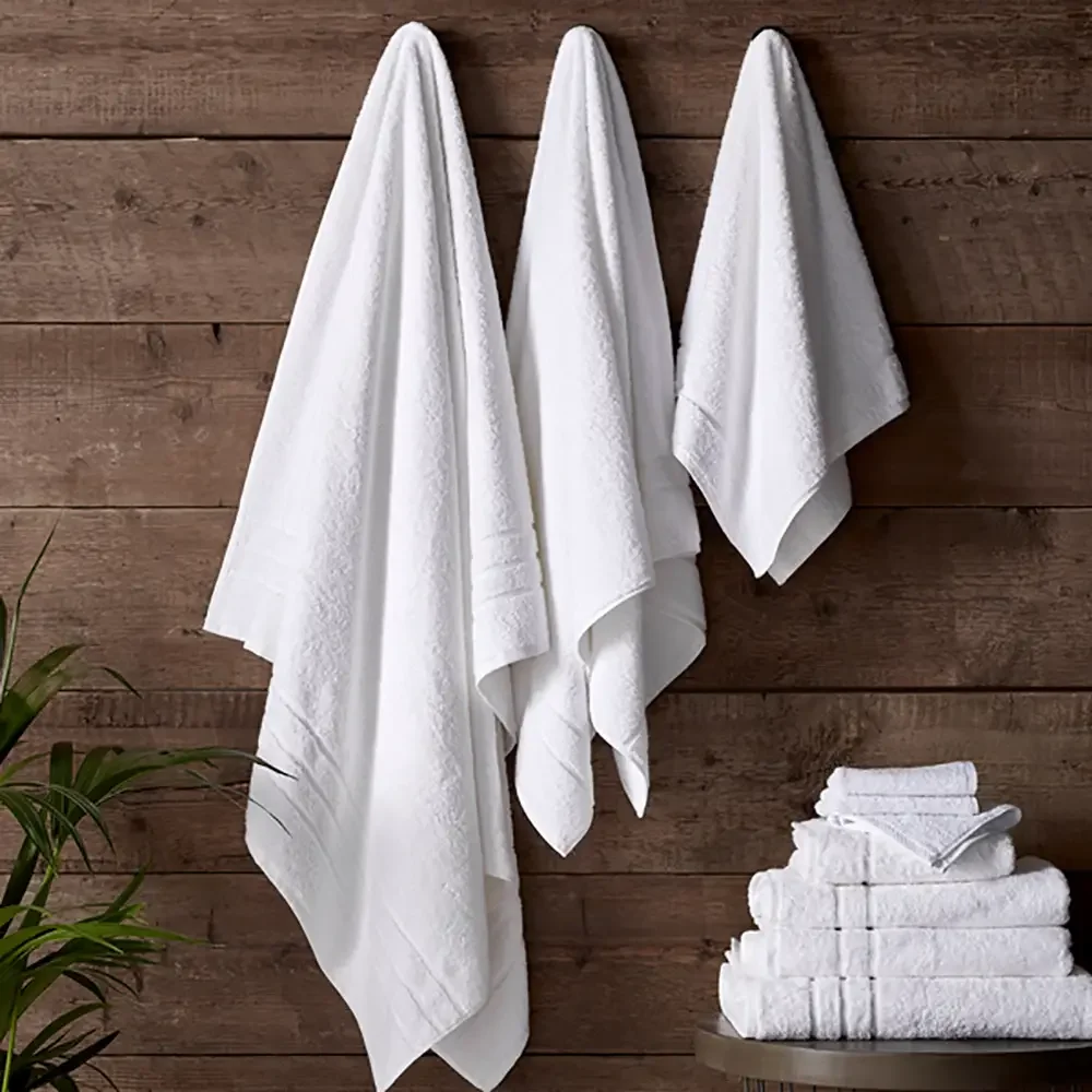 Three white towels hanging on a wooden wall with a stack of folded towels on a small table near the bottom right.