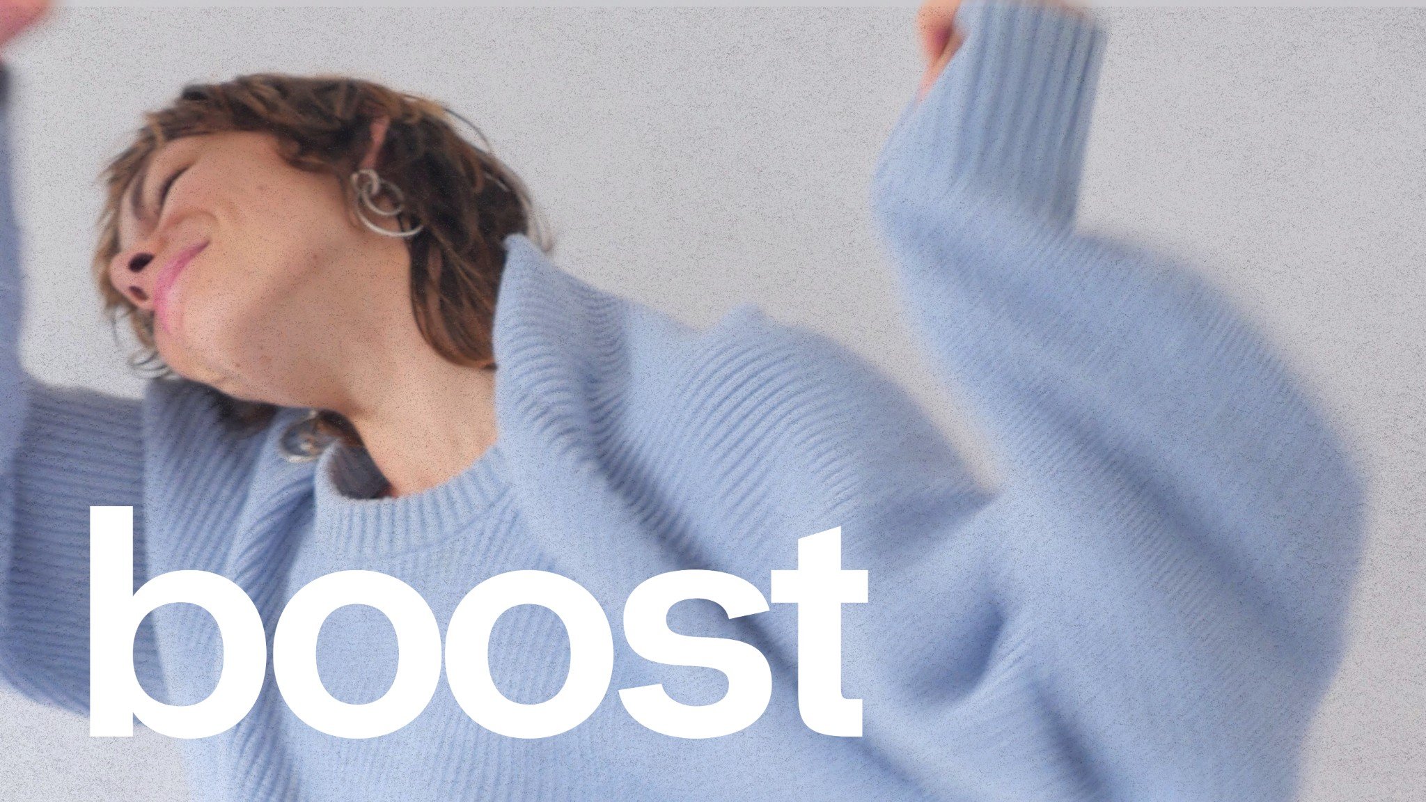 Une jeune femme souriante en pull bleu clair, avec des boucles d'oreilles, tenant ses bras en l'air. Le mot 'boost' écrit en blanc en bas de l'image.