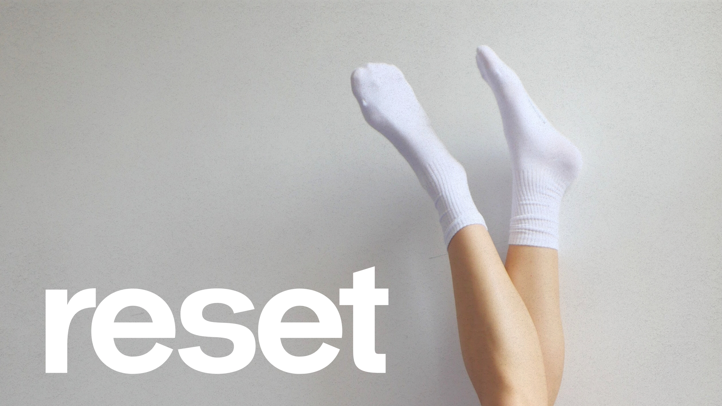 Des jambes avec des chaussettes blanches, les jambes sont levées contre un mur avec le mot 'reset' écrit en blanc en bas à gauche.