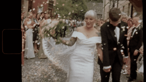 A bride and groom walking under the Bridge of Sighs in Oxford UK at their wedding, surrounded by guests, with celebration confetti falling around them.