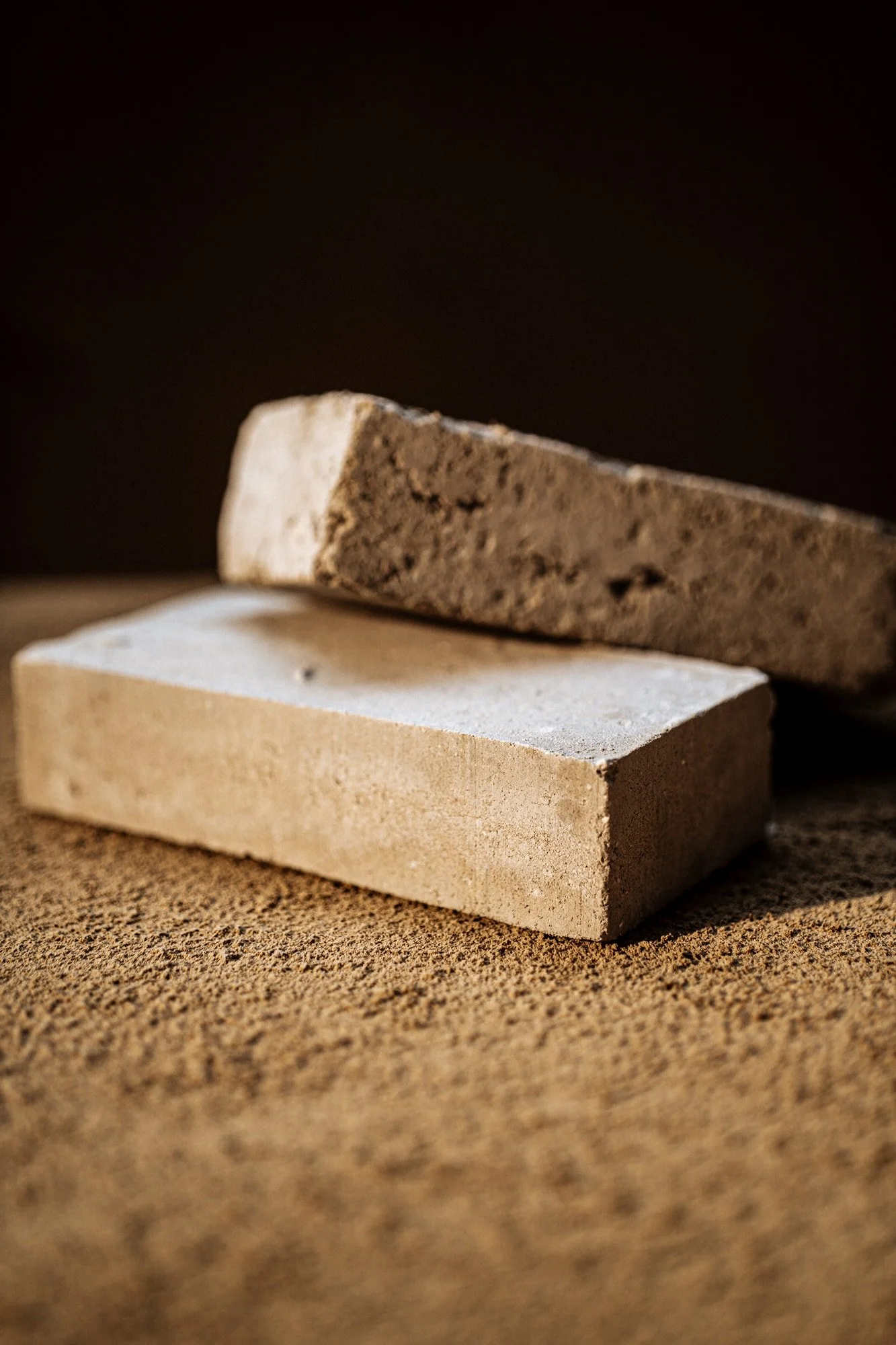 To sten af forskellige materialer, en hvid og en mørk, placeret på en sandbunden overflade mod en mørk baggrund.
