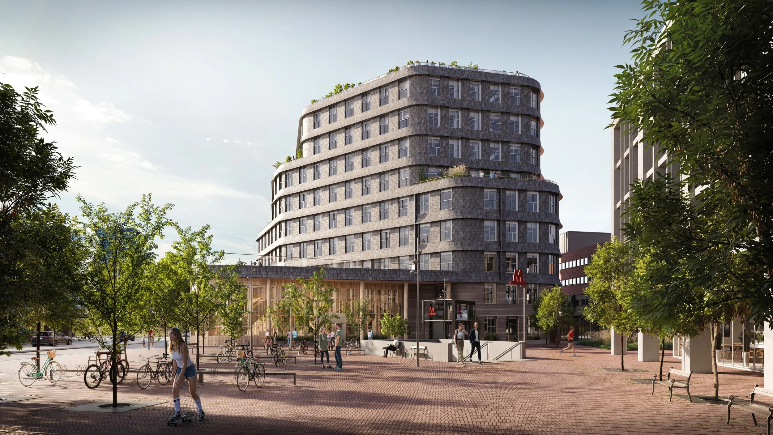 Fritidsområde med mennesker, cykler og et moderne antal bygninger, inklusive en høj lejlighedskompleks med buede facader. Der er træer, bænke og en metrostation til fodgængere.