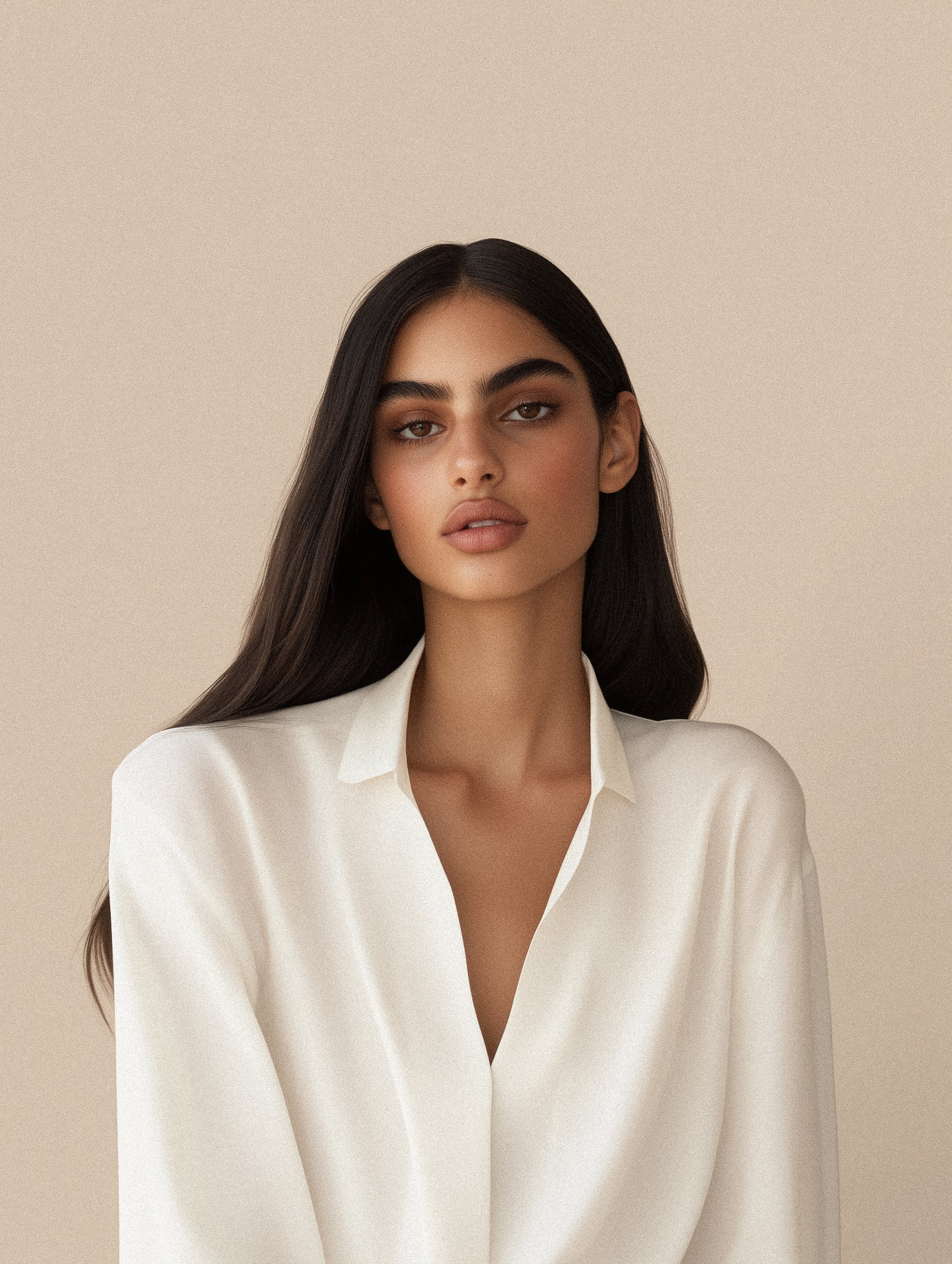 Portrait of a woman with long dark hair wearing a white blouse against a beige background.